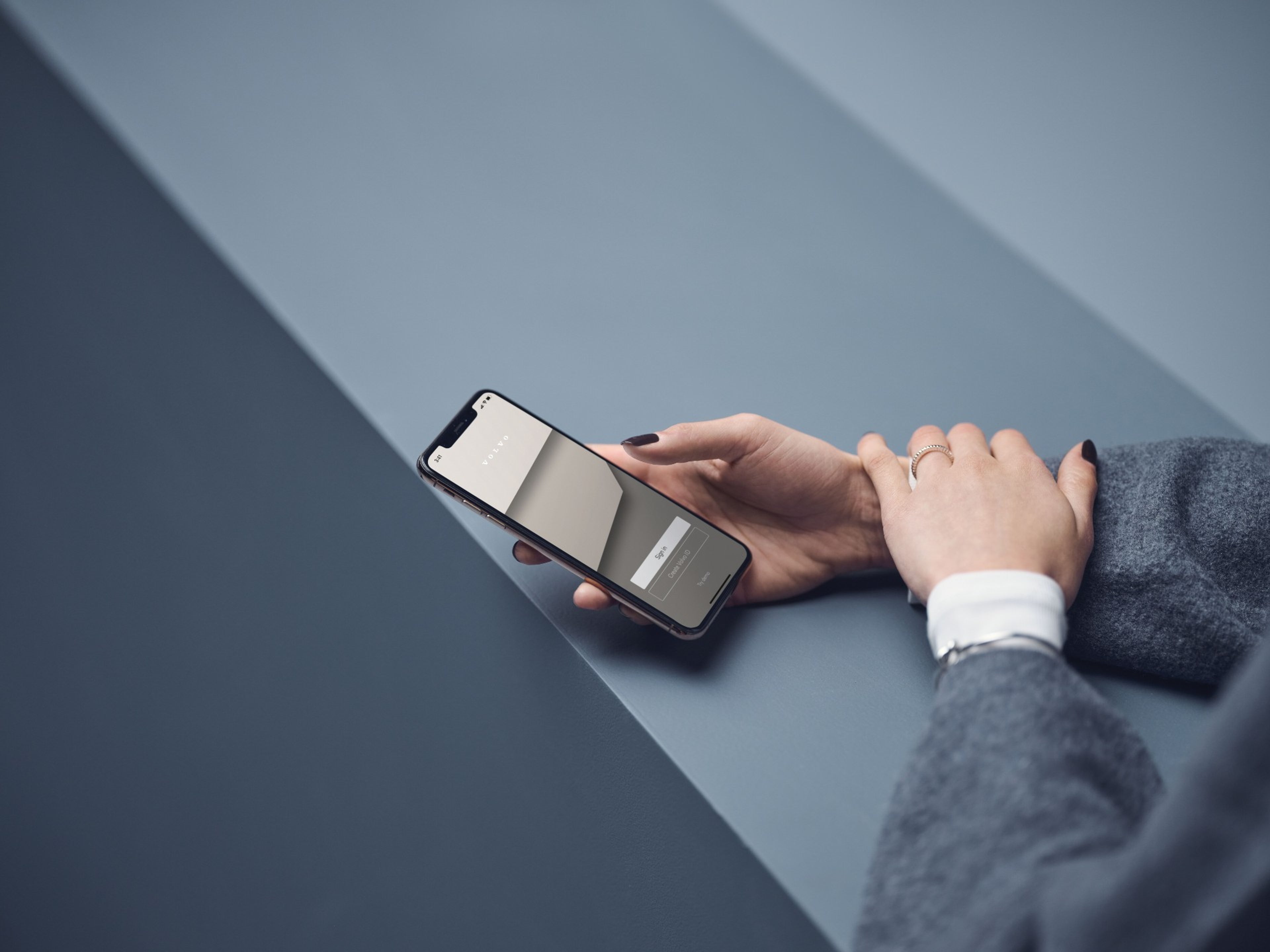 close de uma mão de mulher a segurar um telemóvel com a app volvo aberta, na tela inicial