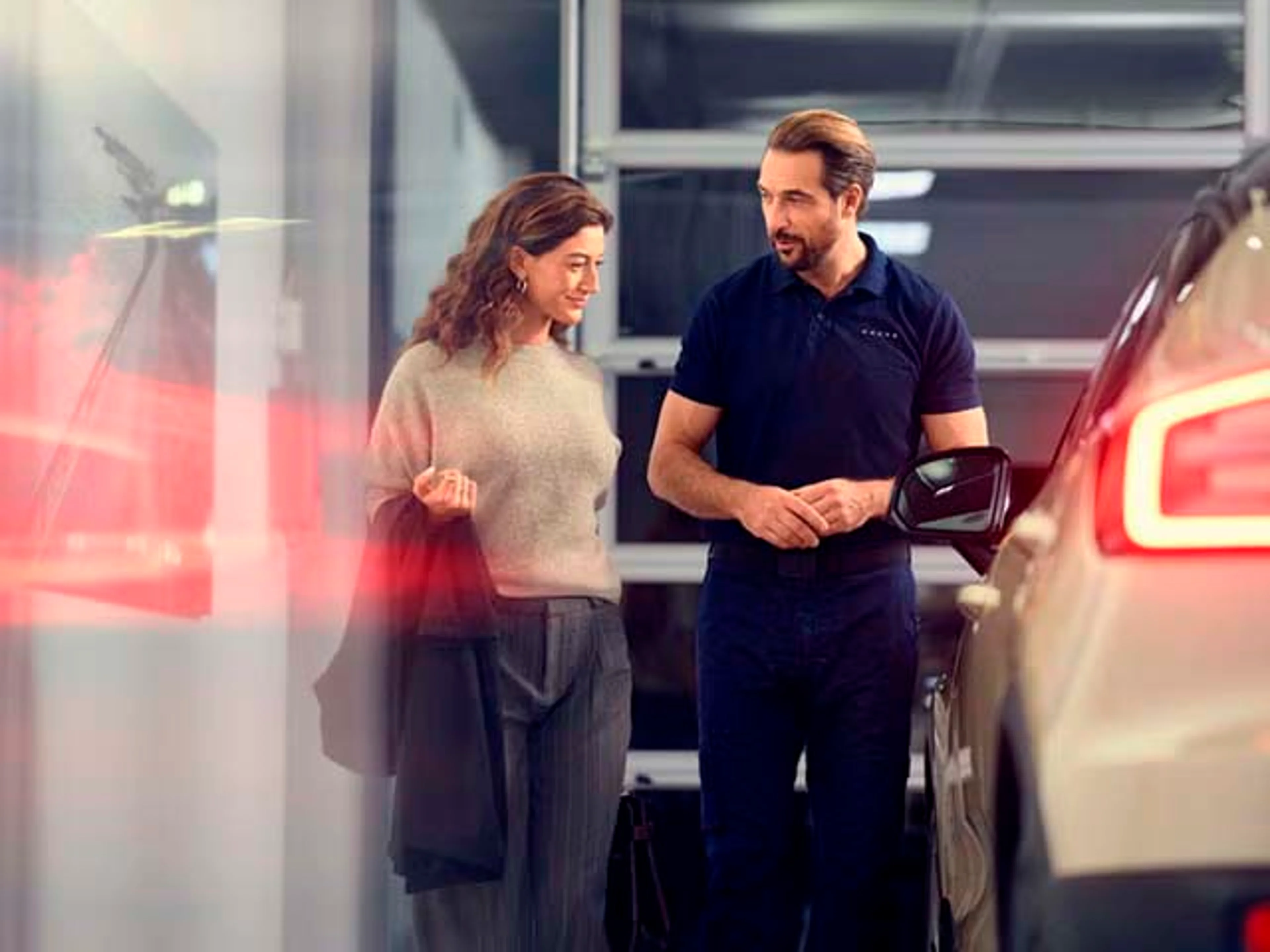 Un técnico de Volvo conversando con una cliente en un servicio oficial Volvo mientras pasan al lado de vehículos