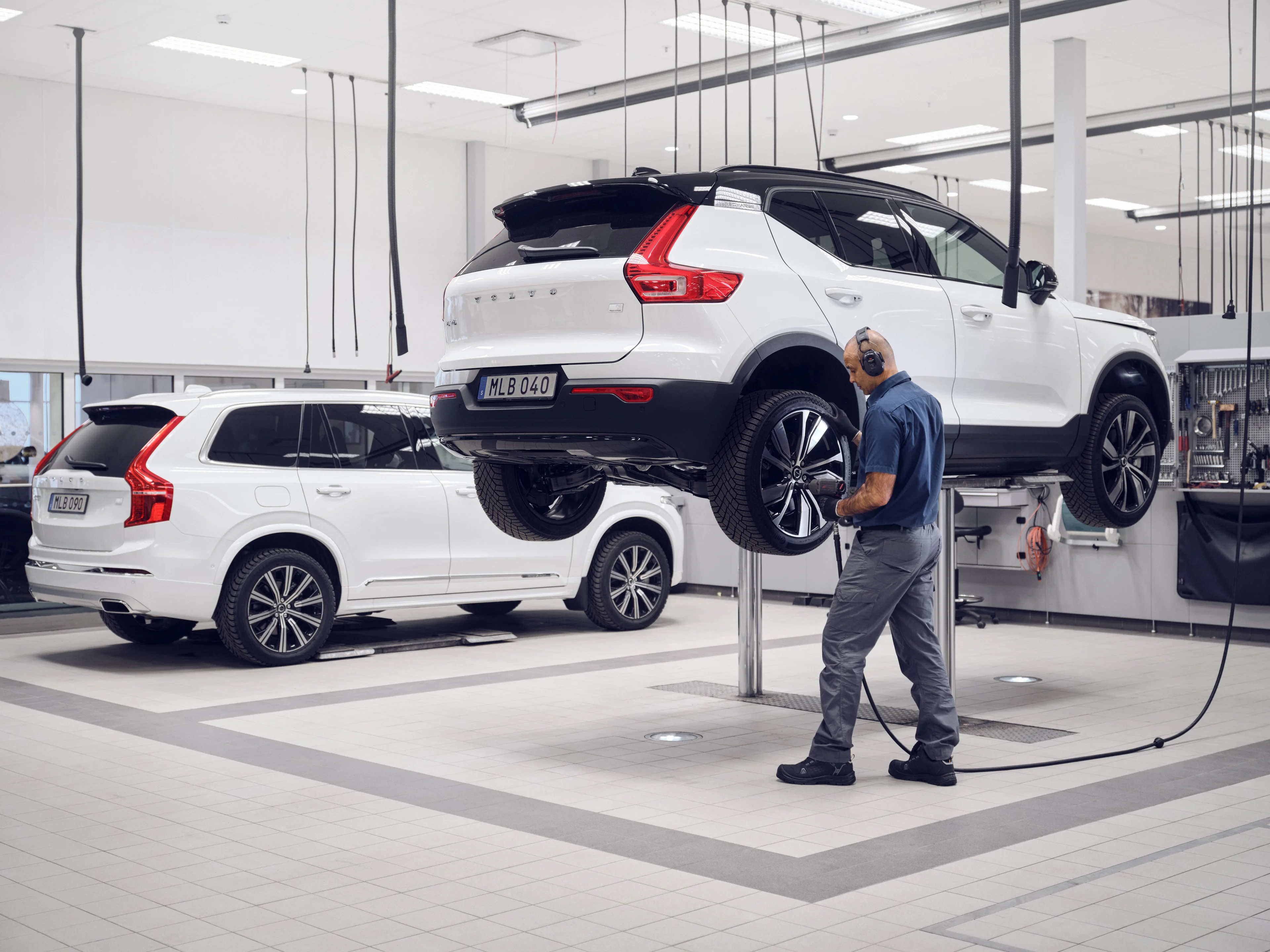 Oficina Volvo com um XC90 branco e um C40 no elevadro, juntamente com um tecnico.