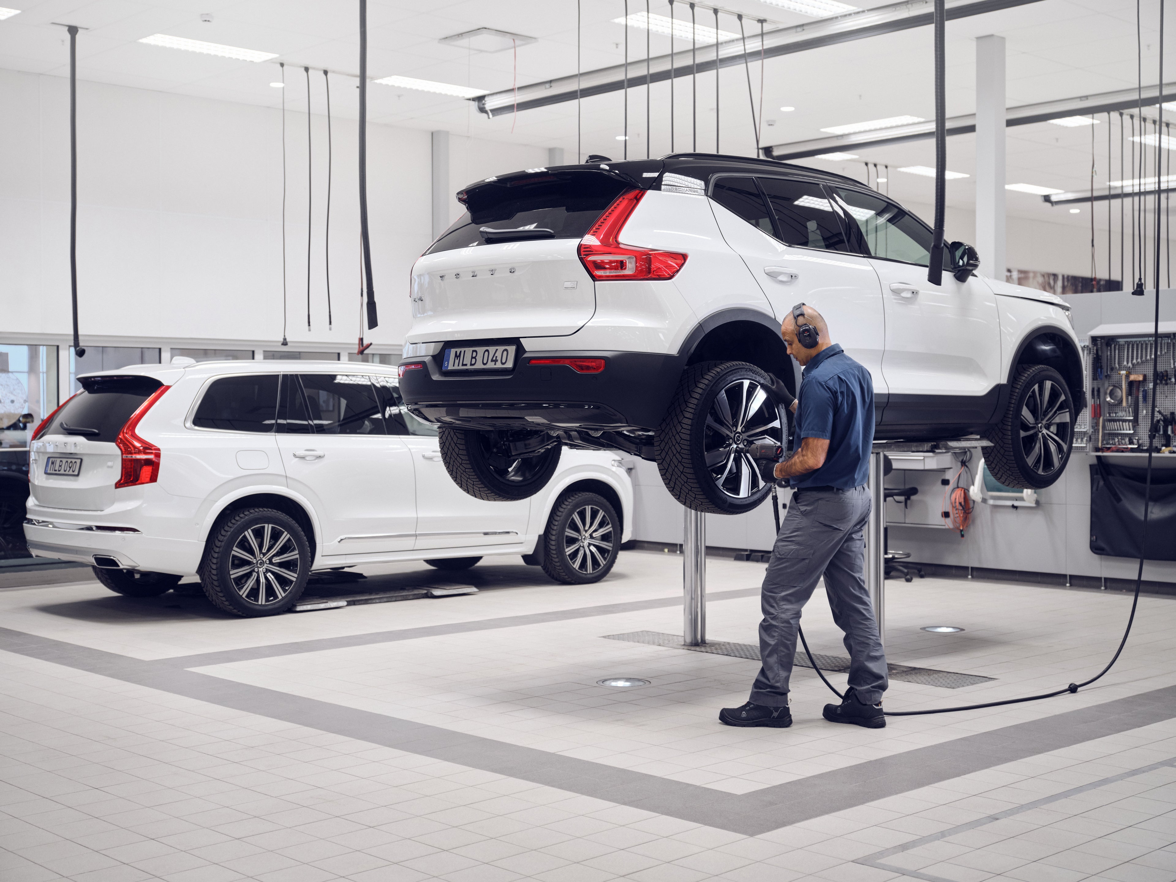 Oficina Volvo com um XC90 branco e um C40 no elevadro, juntamente com um tecnico.