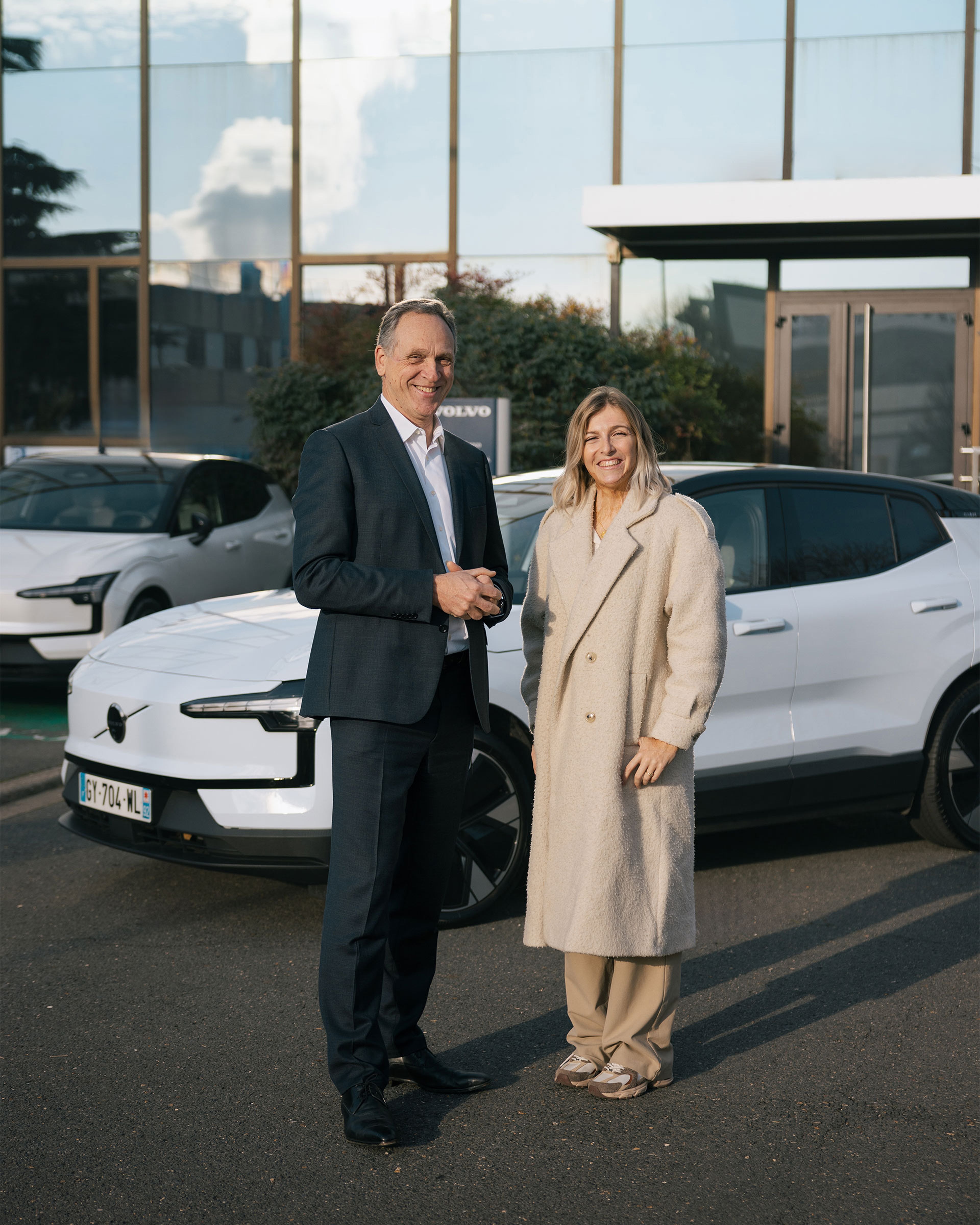 Julie Bourges et Yves Pasquier-Desvignes devant une concession Volvo avec deux voitures blanches en arrière-plan