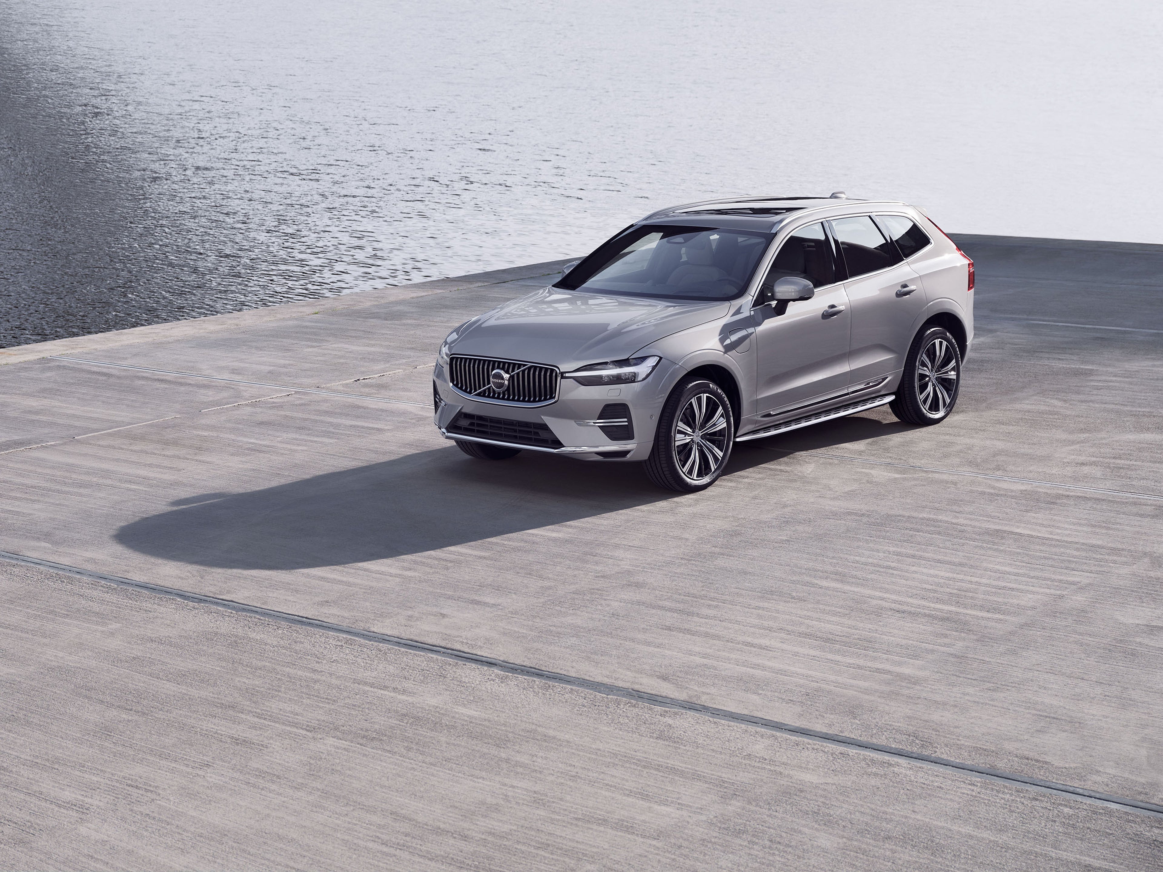 Grijze Volvo XC60 in de zomer bij water. De zon schijnt.