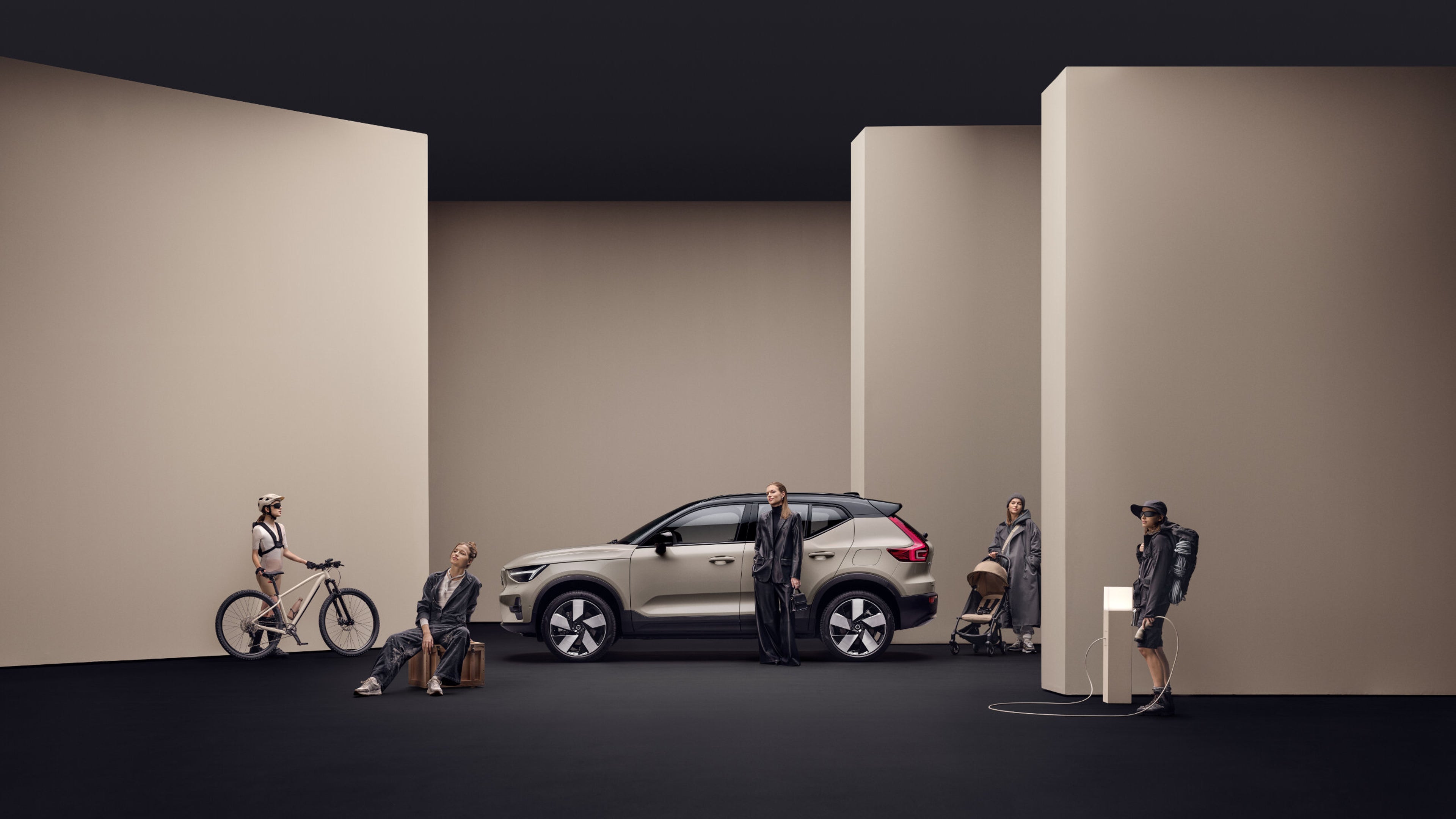 Seitenansicht eines beigen Volvo EX40, um den Personen herumstehen.