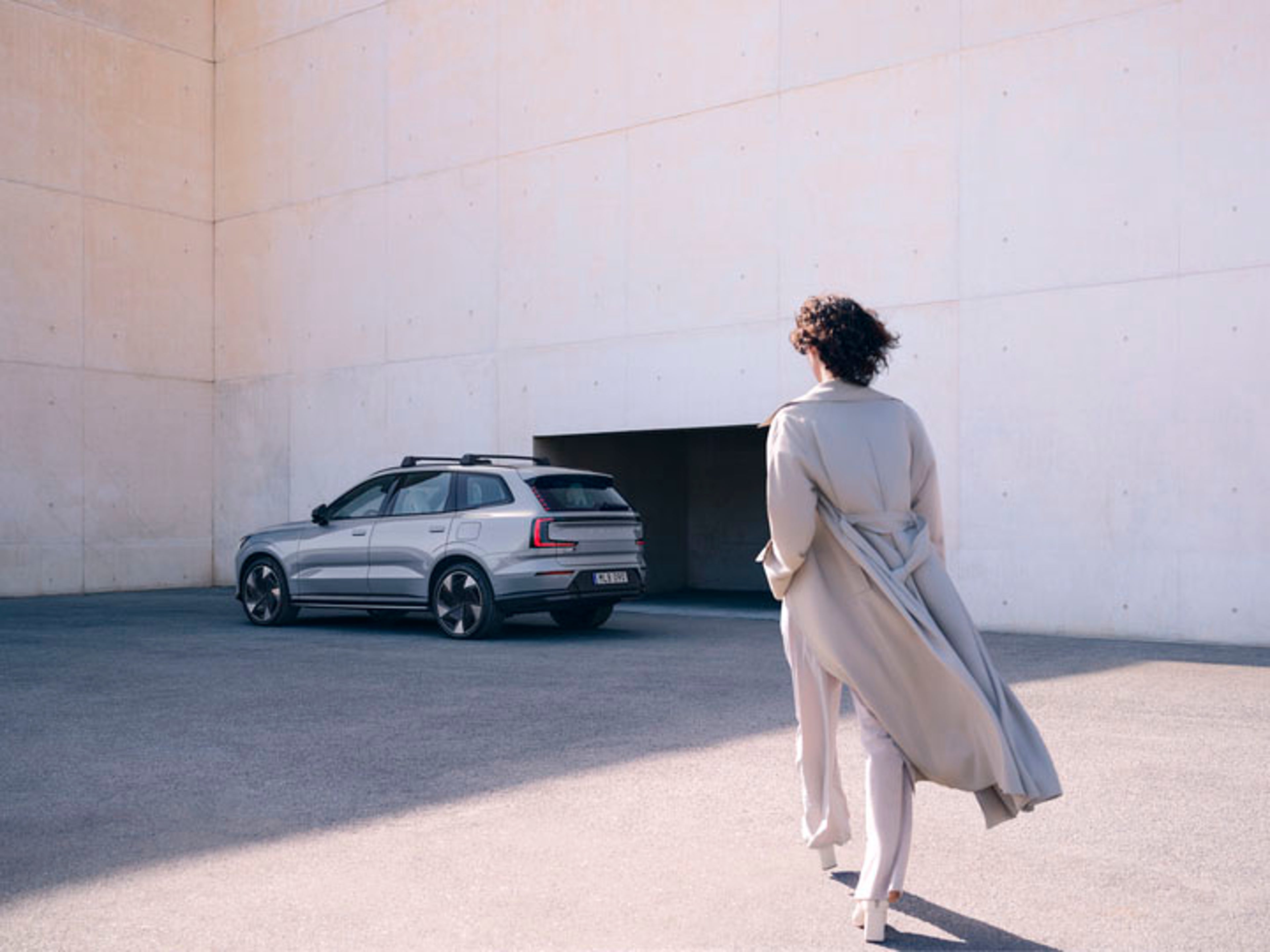 Una mujer andando hacia un Volvo eléctrico color plateado