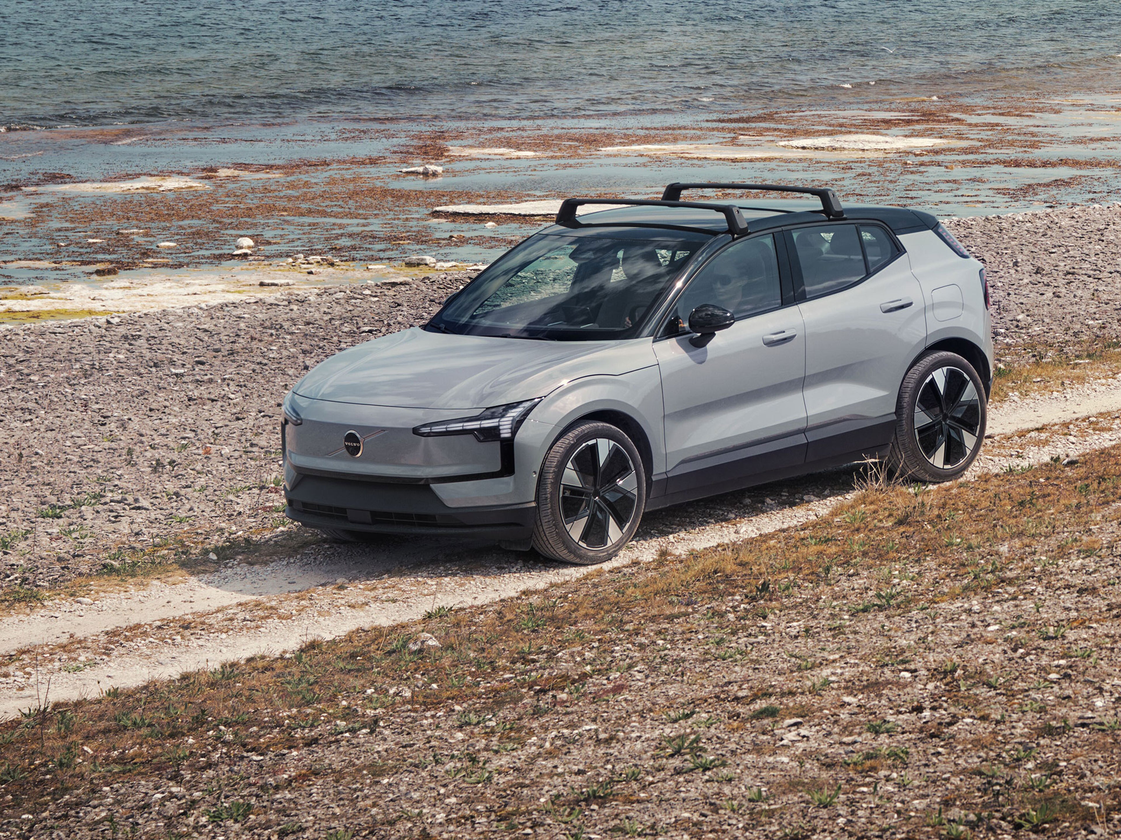 Cloud Blue -värinen Volvo EX30 täyssähköauto ajaa hiekkaisella rantatiellä.