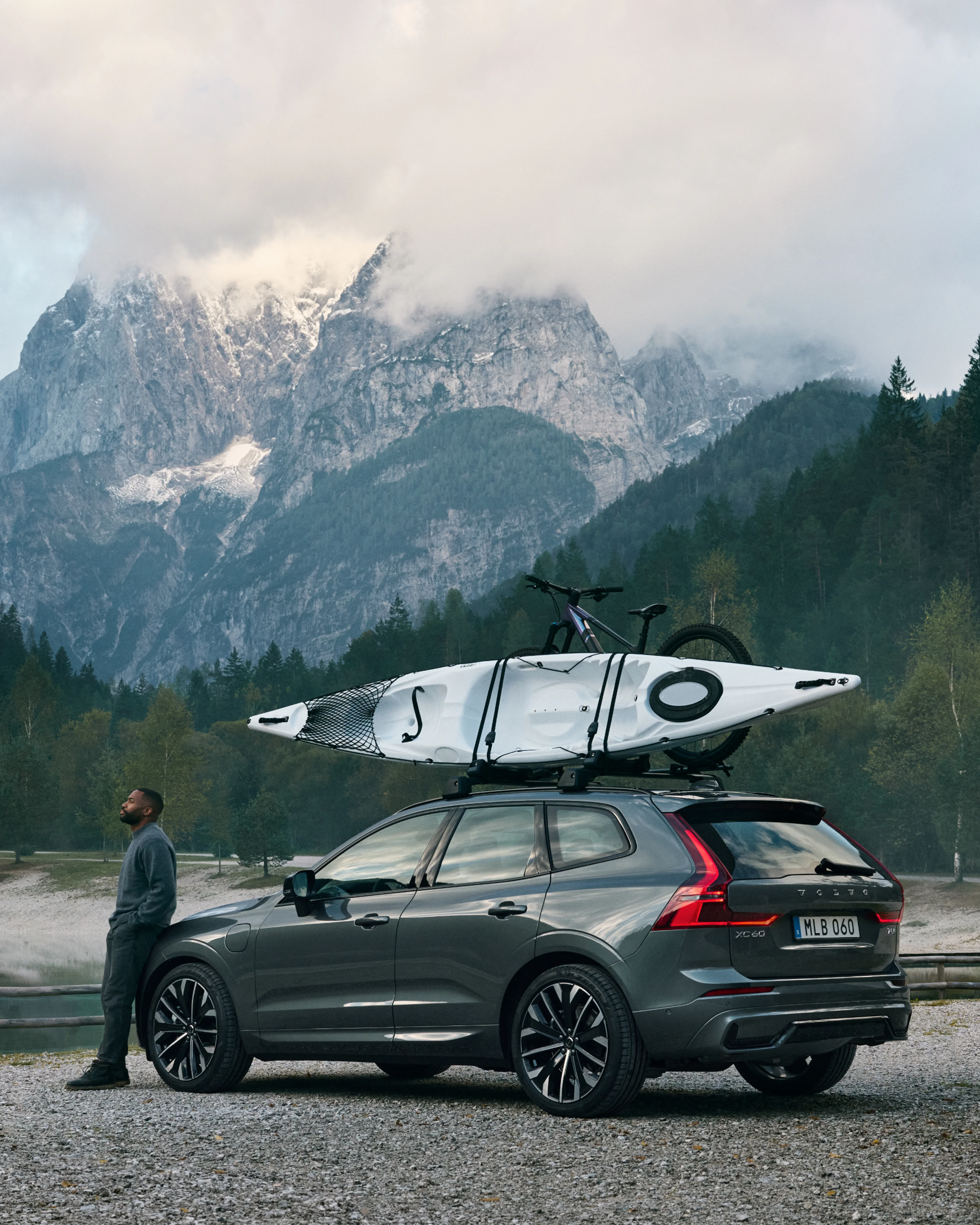 Der Volvo XC60 in der Farbe Forest Lake (dunkelgrün) steht im Wald vor einem See.