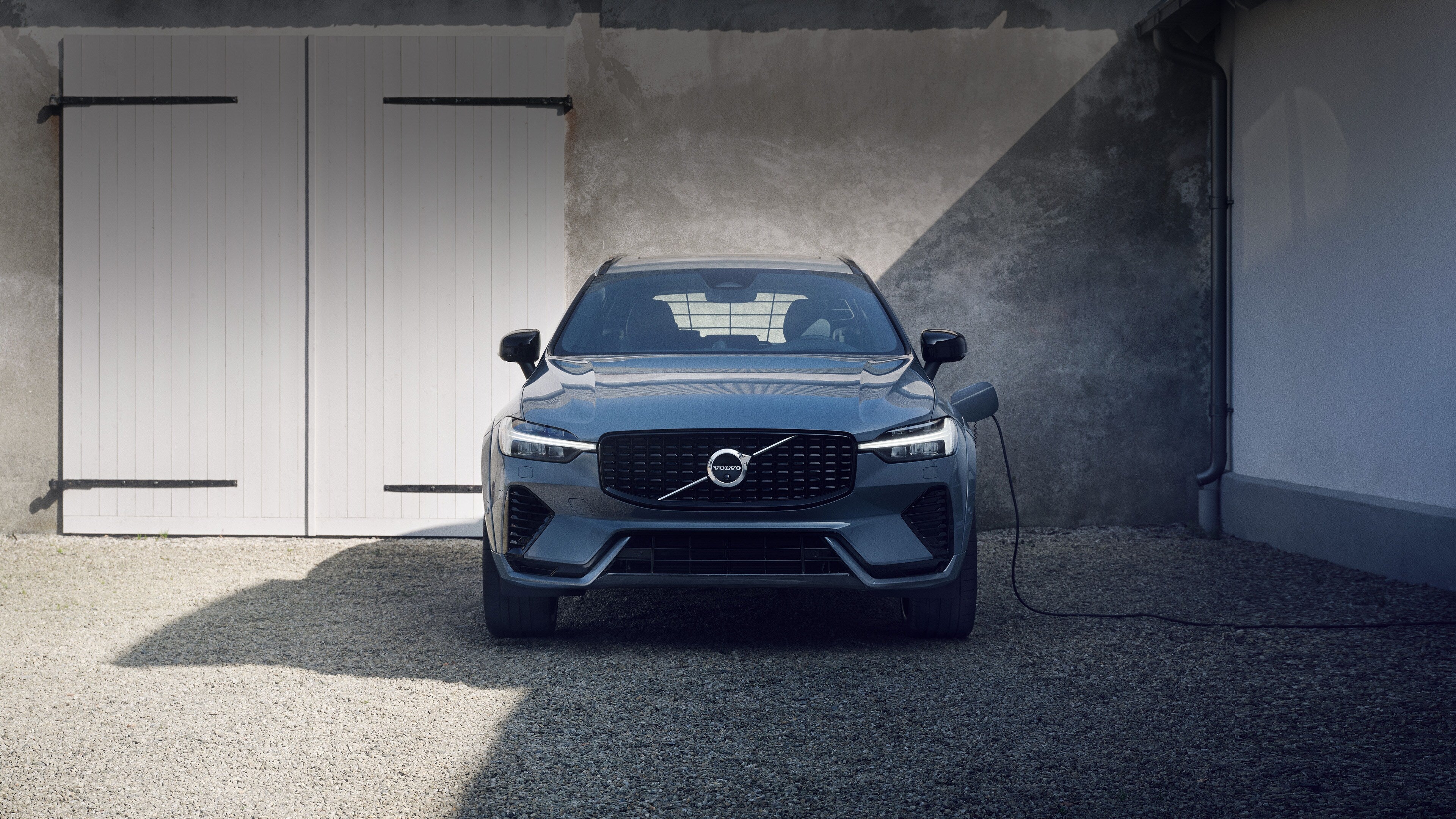 En elegant grå Volvo elbil er parkeret og tilsluttet opladning foran en garage med blødt lys, hvilket signalerer moderne effektivitet.