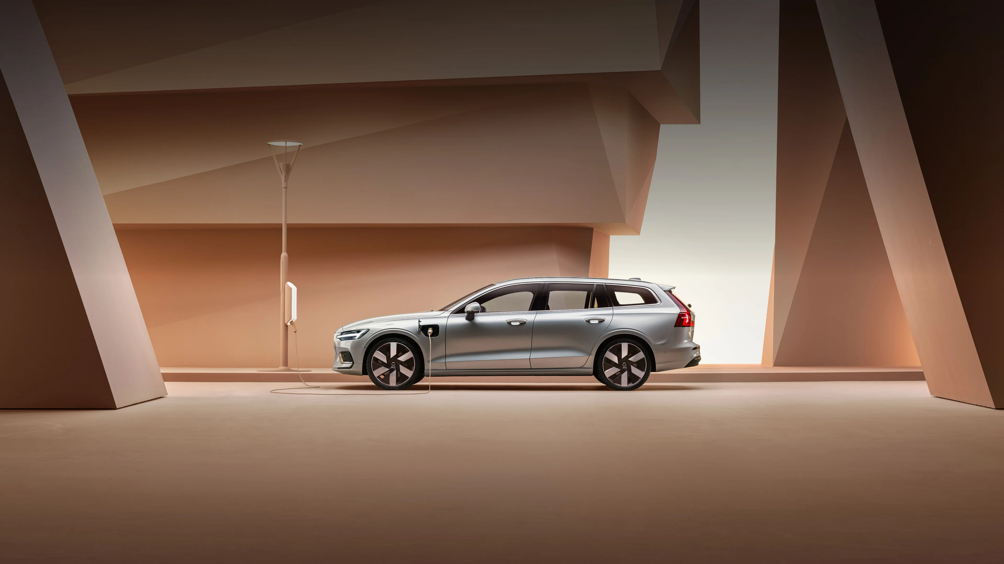 A side profile image of the Volvo V60 plug-in hybrid in silver dawn. Parked against an orange backdrop.