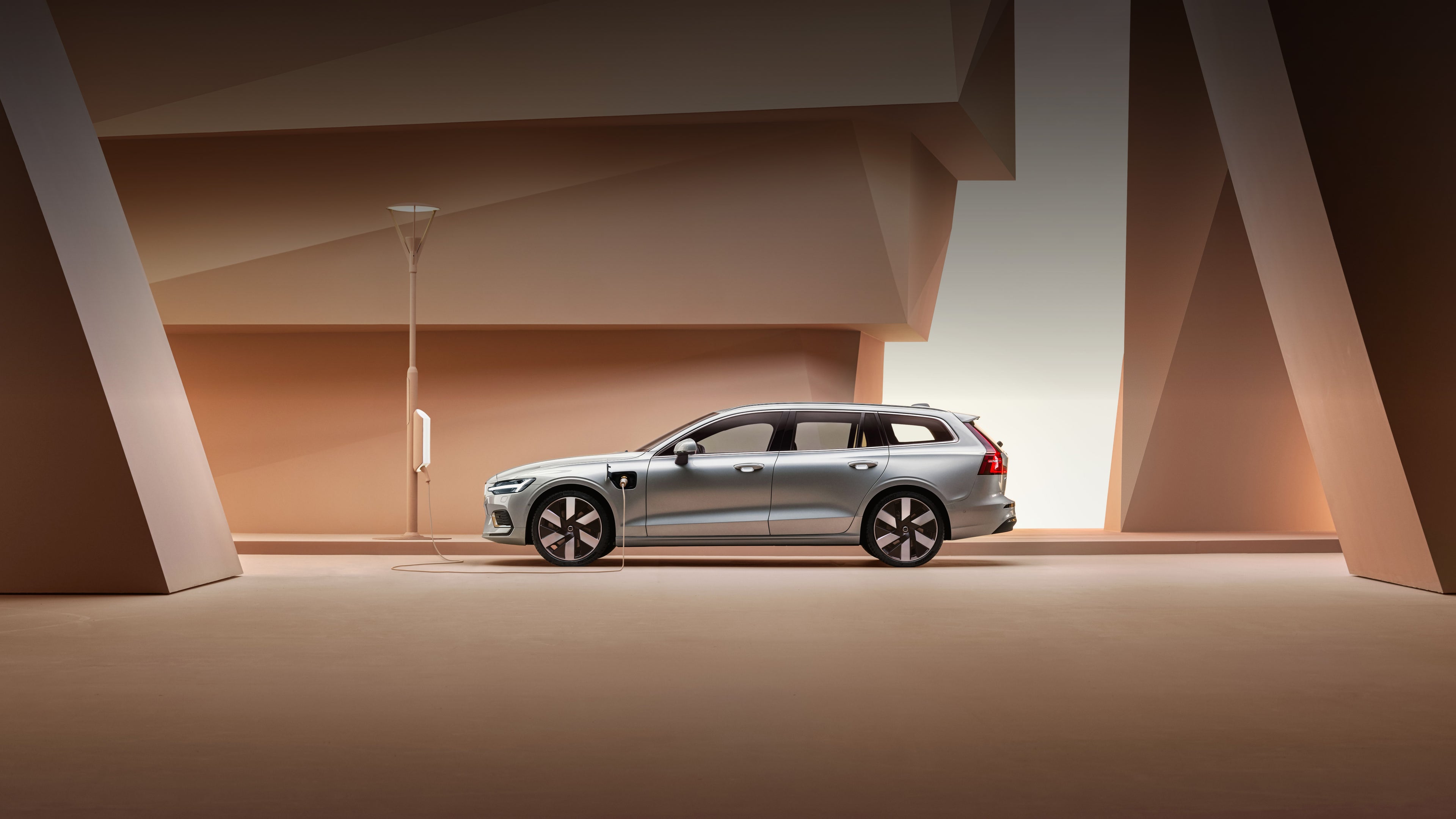 A side profile image of the Volvo V60 plug-in hybrid in silver dawn. Parked against an orange backdrop.