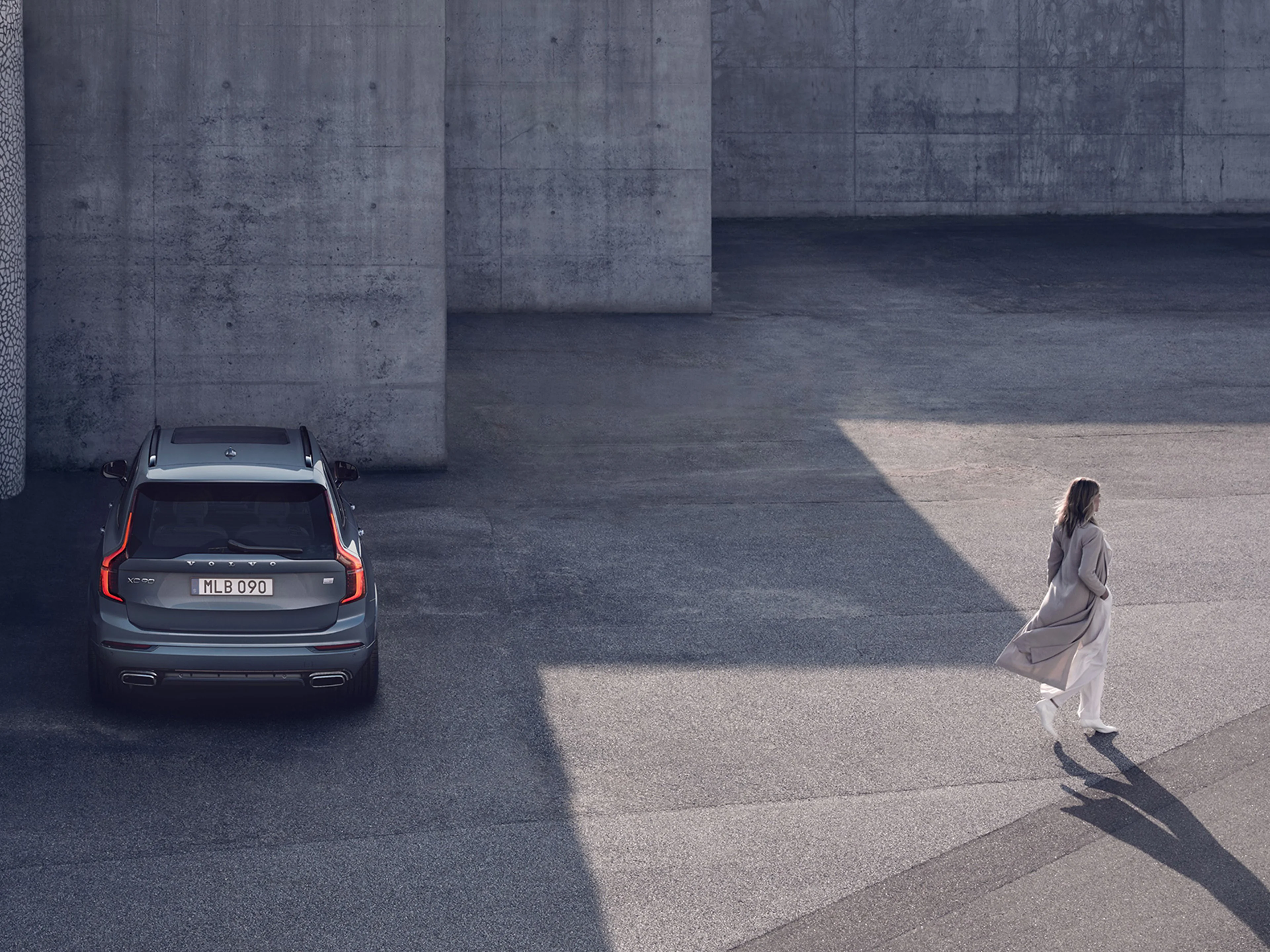 Eine blonde Frau im Mantel entfernt sich von ihrem blauen Volvo XC90.