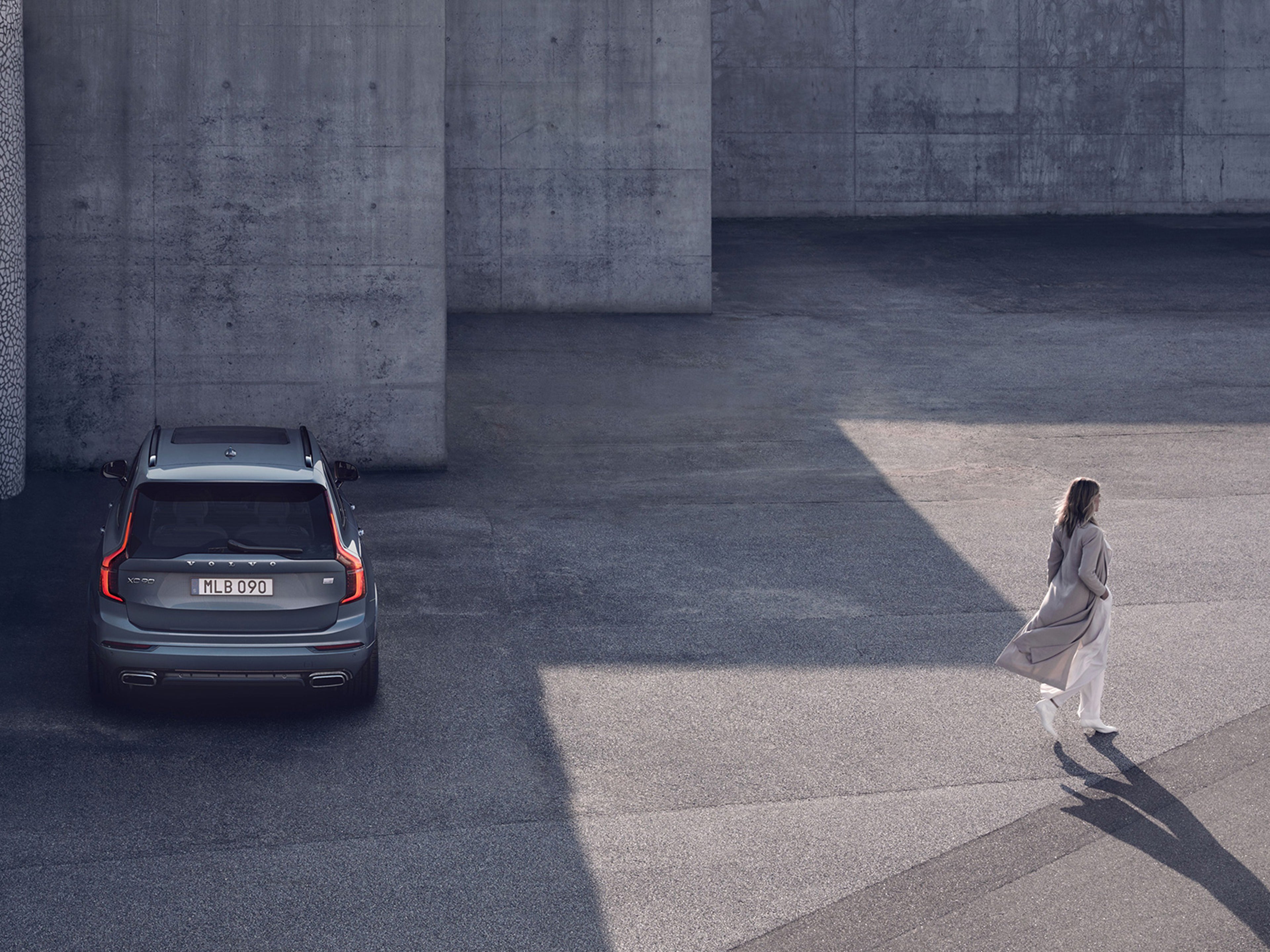 Eine blonde Frau im Mantel entfernt sich von einem silbernen Volvo XC90.