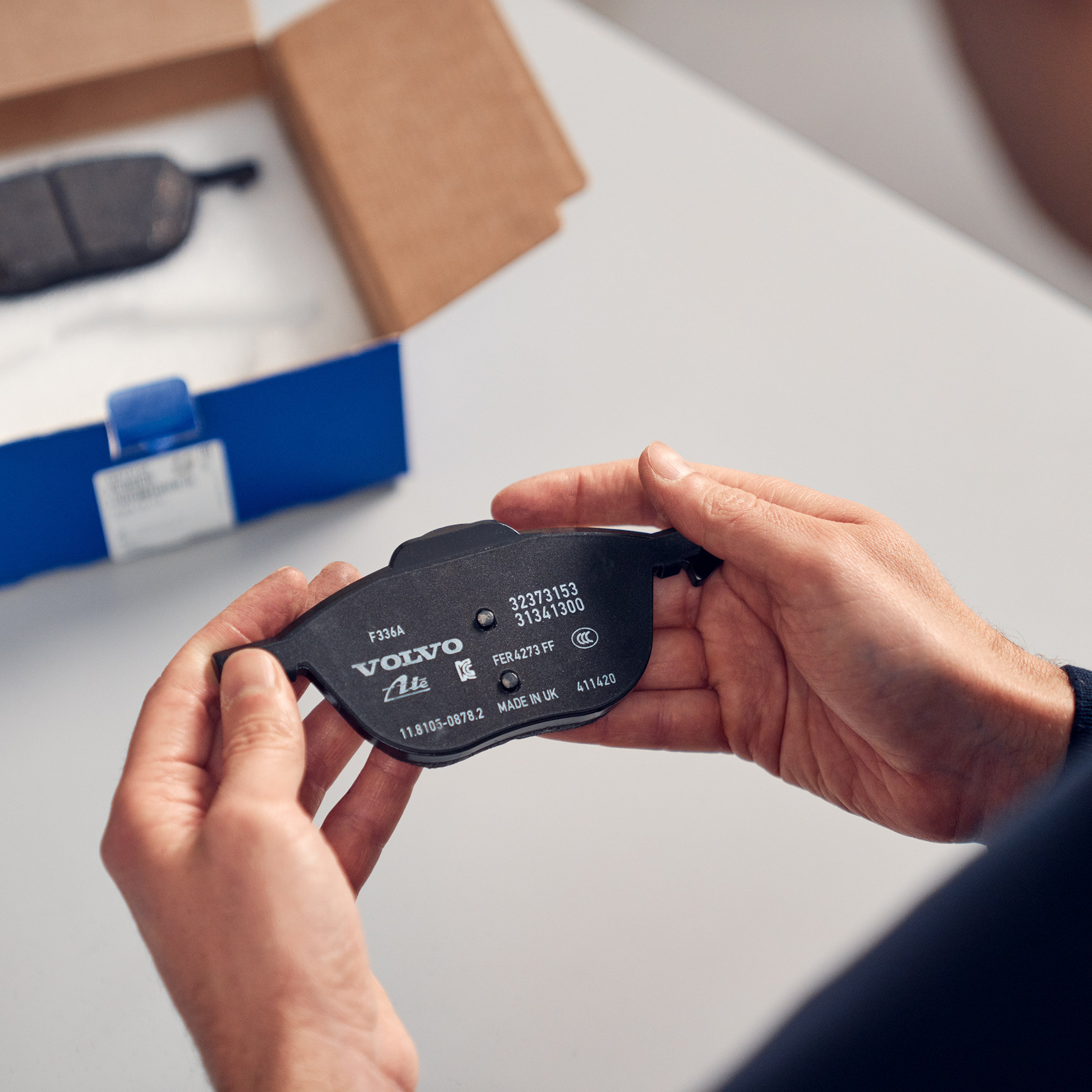 Volvo Omamekaanikko pitää kädessään pakkauksesta esille otettua otettua Volvo Alkuperäinen varaosa jarrupalaa.