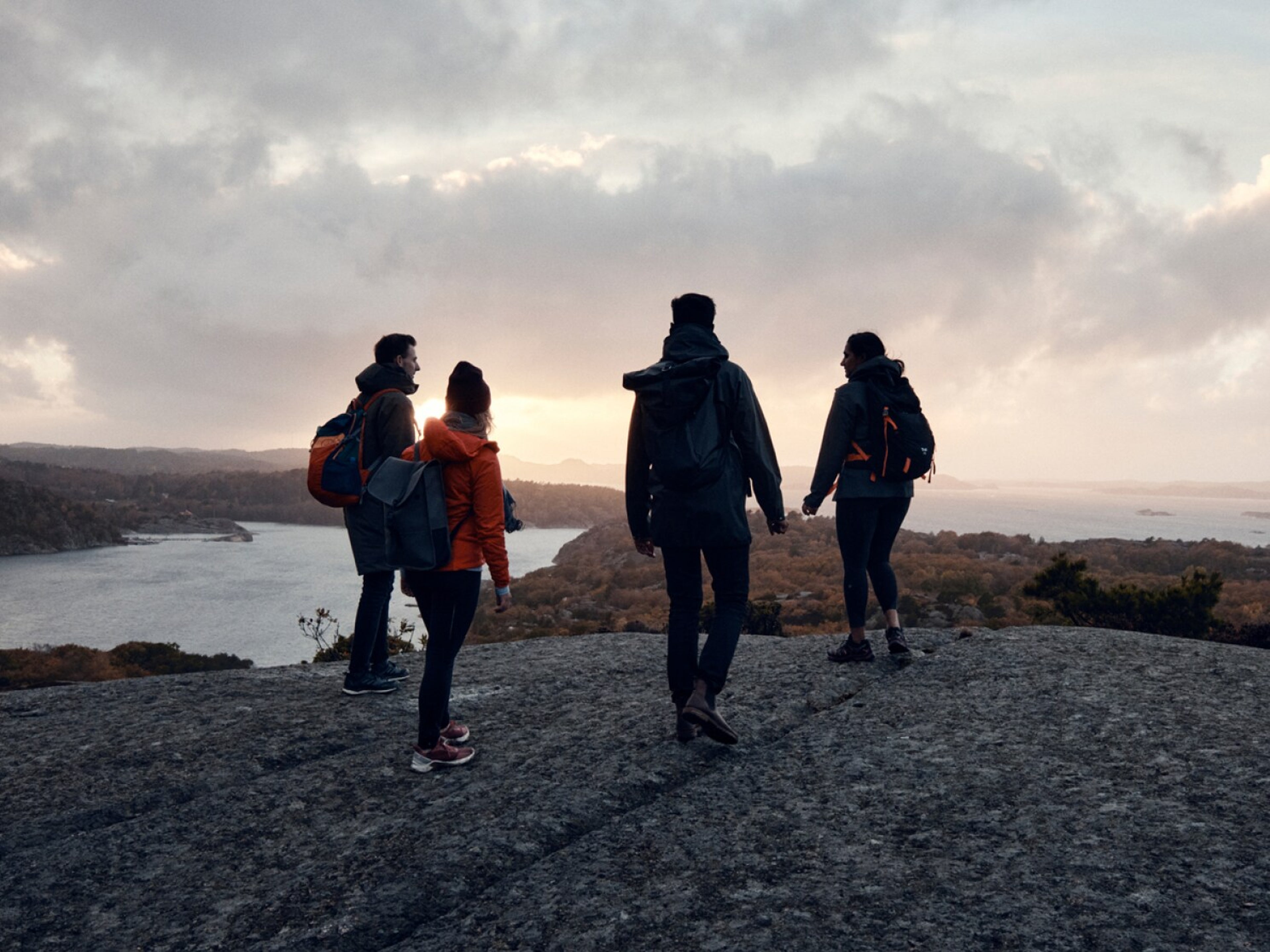 Štyria ľudia na vrchole útesu sledujú zapadajúce slnko.