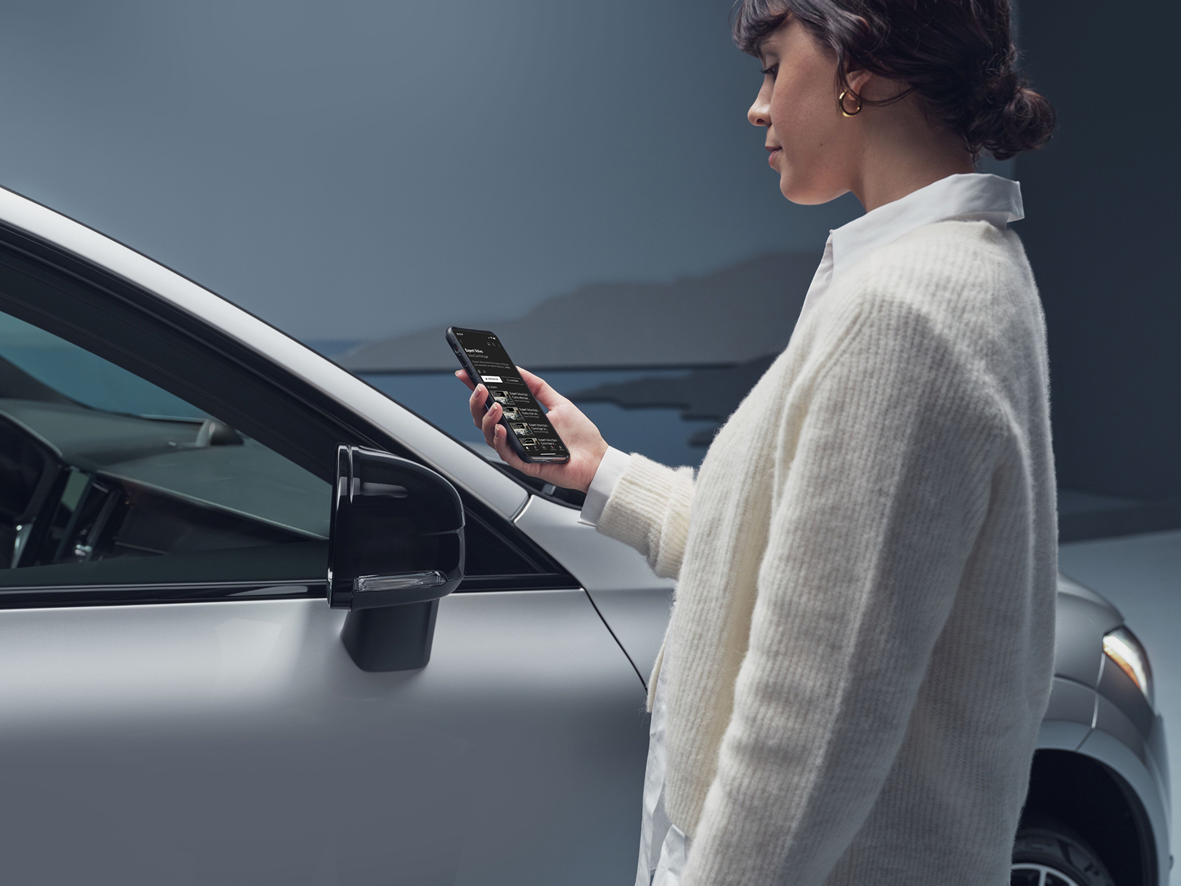 Mulher vestida de branco com o seu telemóvel junto a um volvo