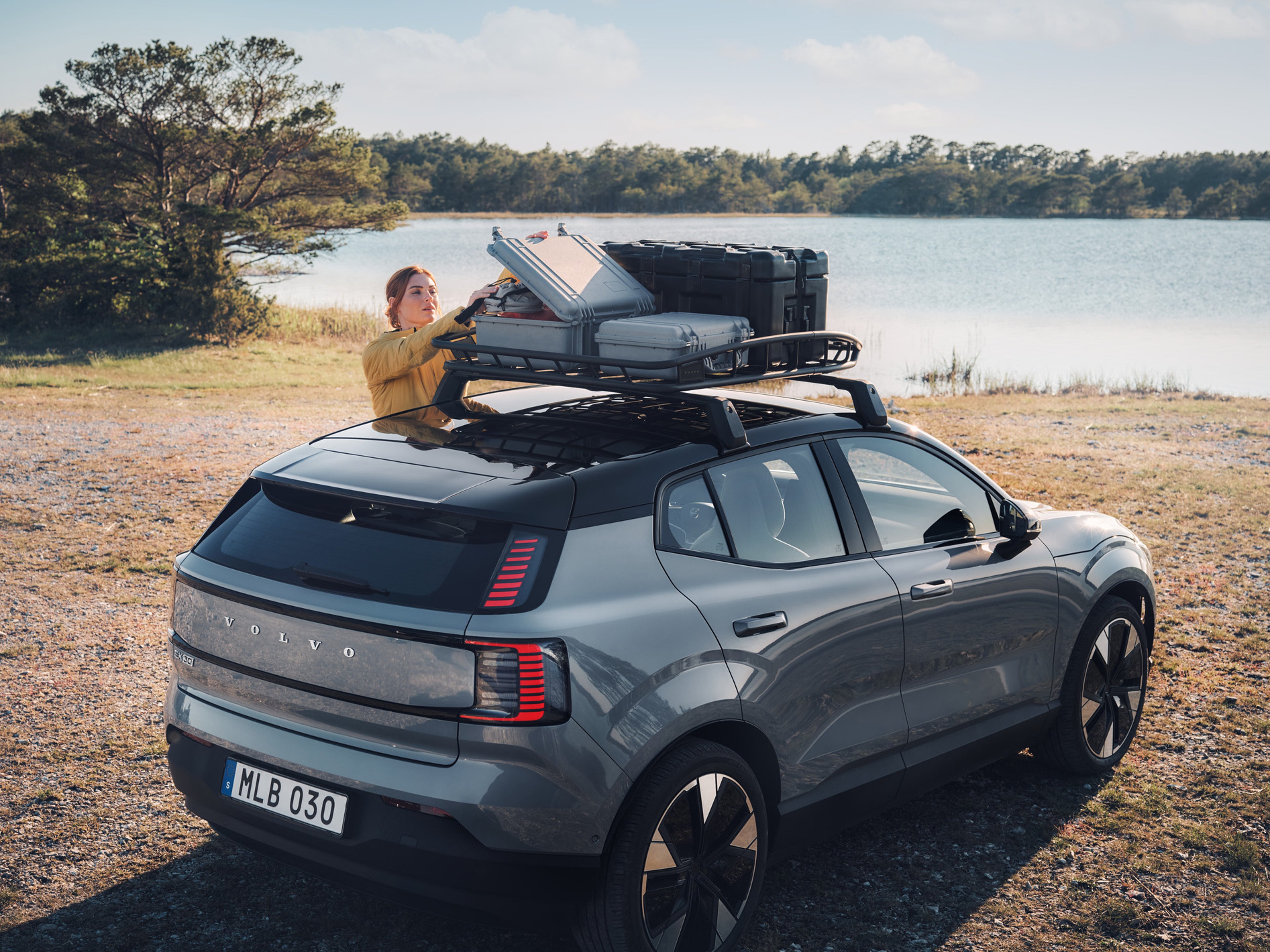 Someone loading roof rack of Volvo EX30 in front of a lake