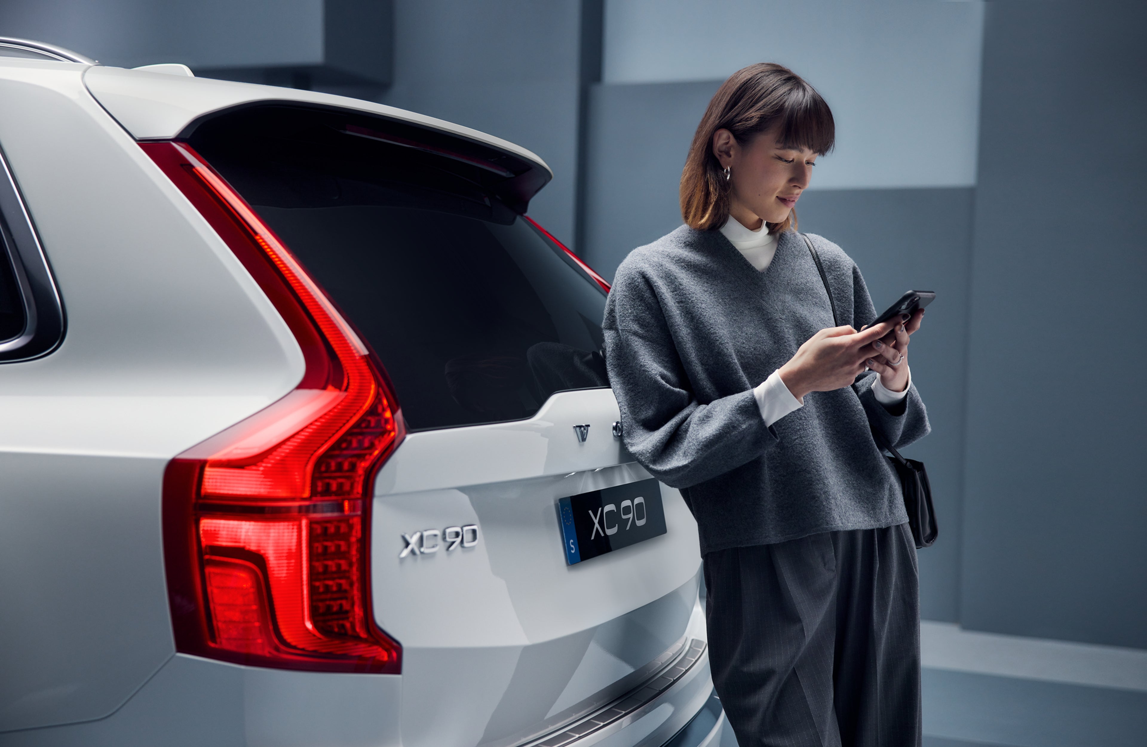 Dame lener seg inntil bagasjeluken på en hvit XC90, studiomiljø.