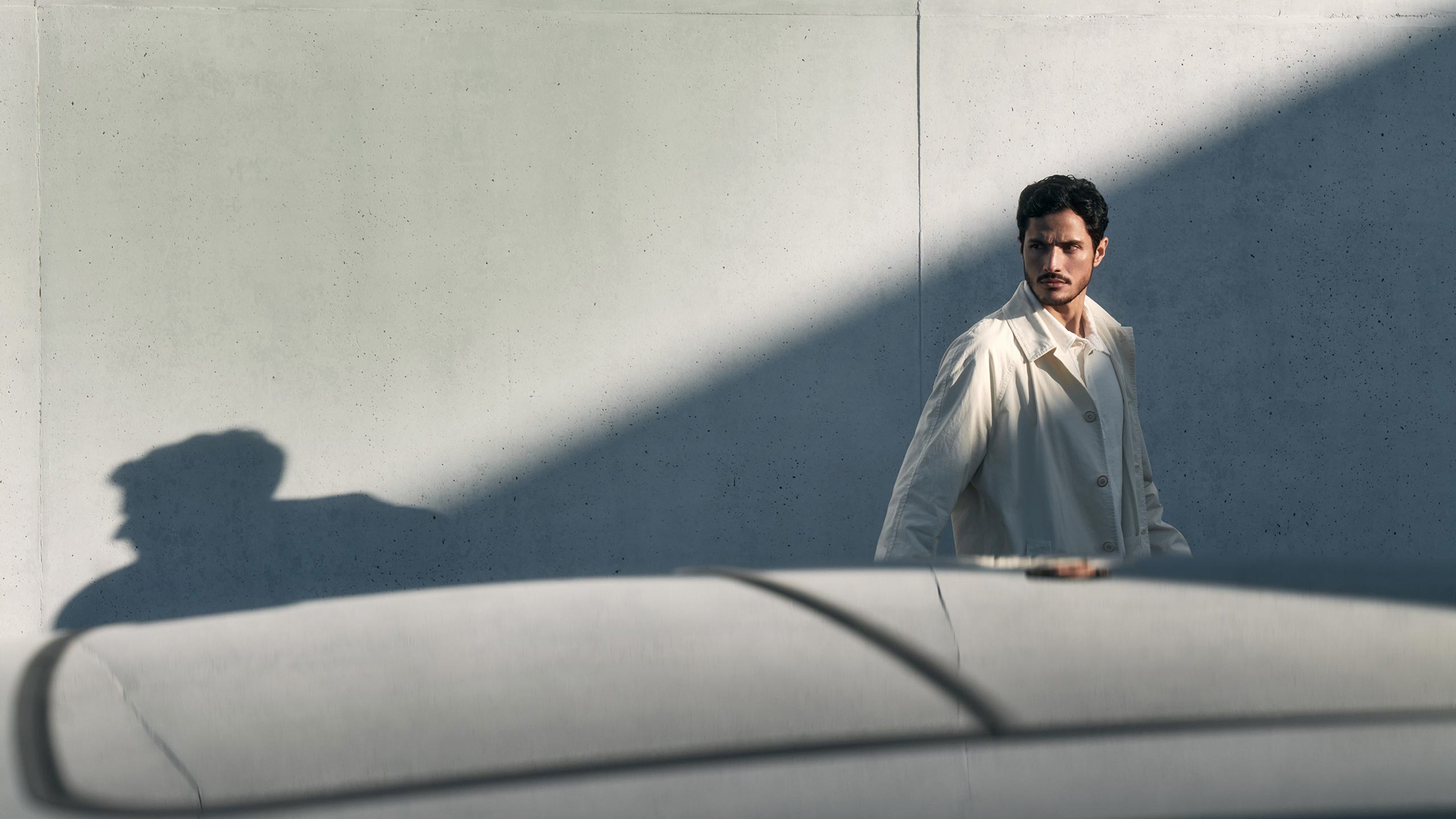 Ein Mann ist ganz in weiß gekleidet und geht hinter einem Wagen entlang.