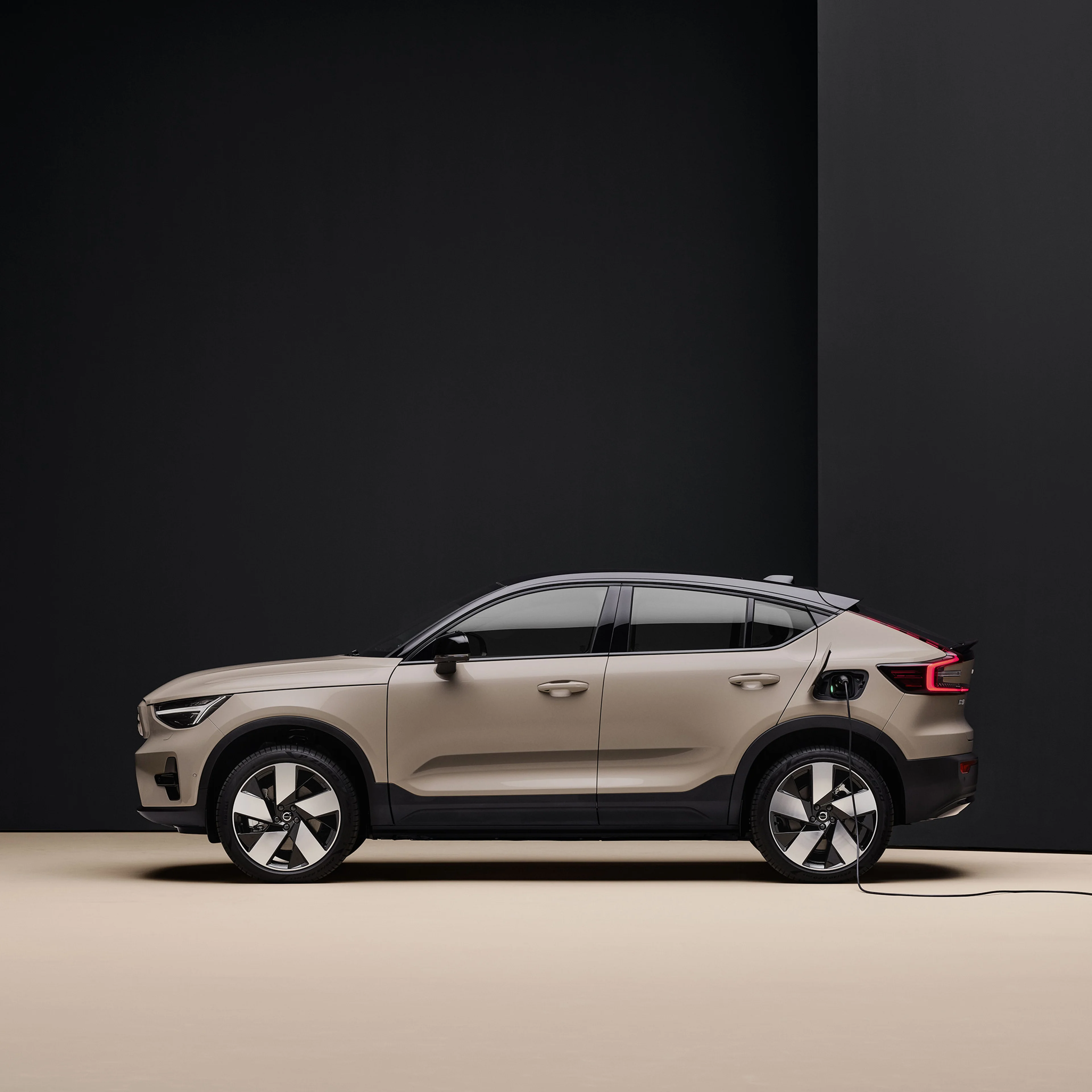 A side view of a sand dune fully electric Volvo EC40 charging at an indoor station, set against a sleek, minimalist black and beige backdrop.