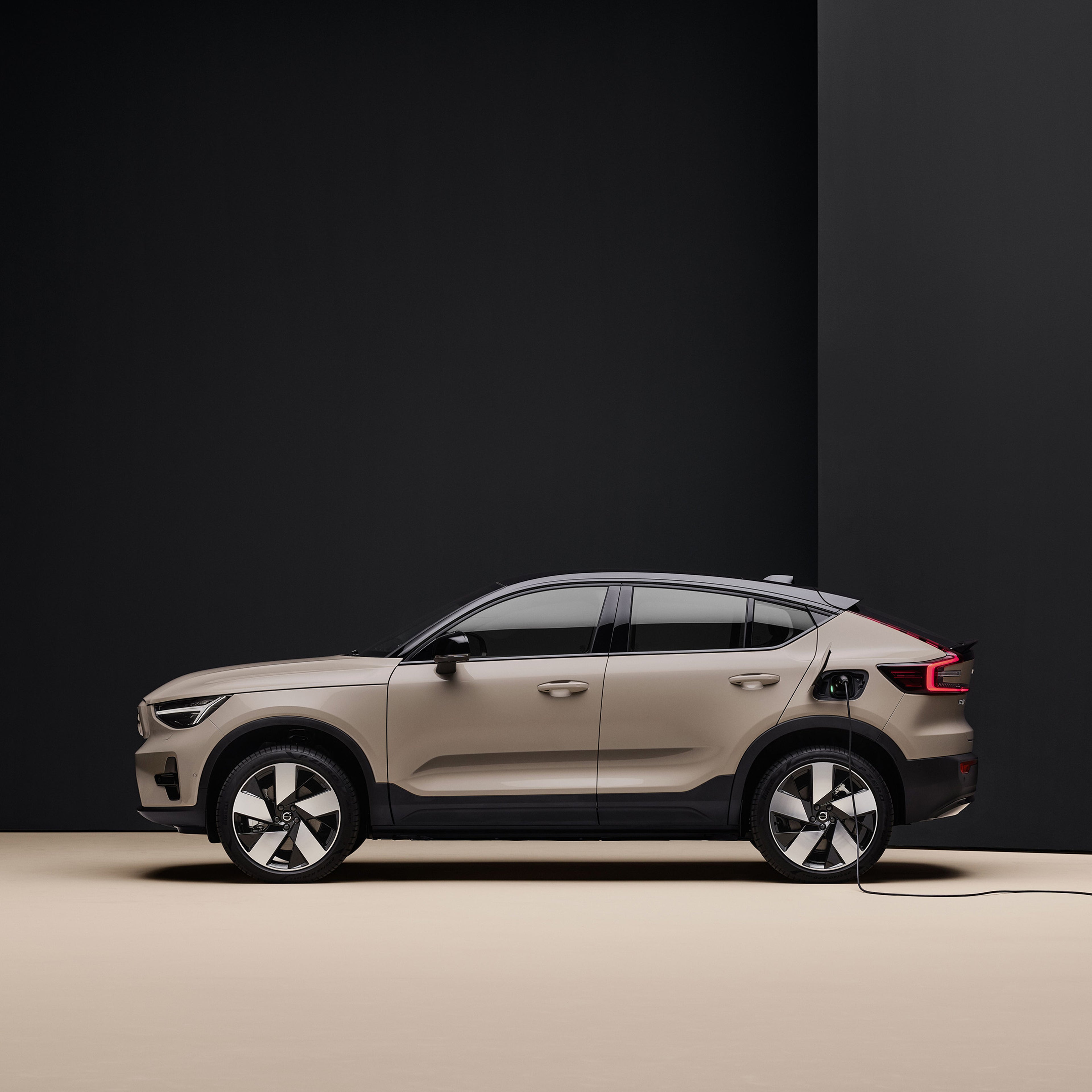 A side view of a sand dune fully electric Volvo EC40 charging at an indoor station, set against a sleek, minimalist black and beige backdrop.