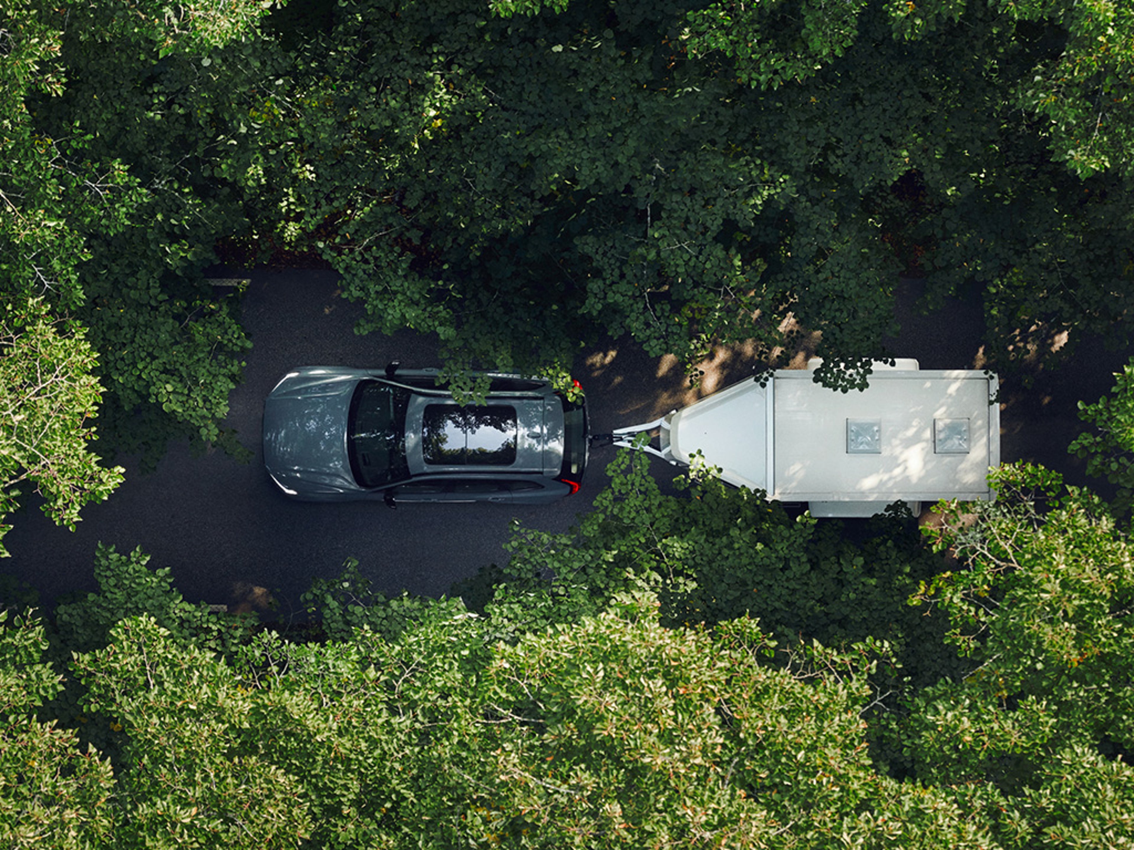 An overhead aerial shot of the Volvo XC60 plug-in hybrid towing a trailer through a forest.