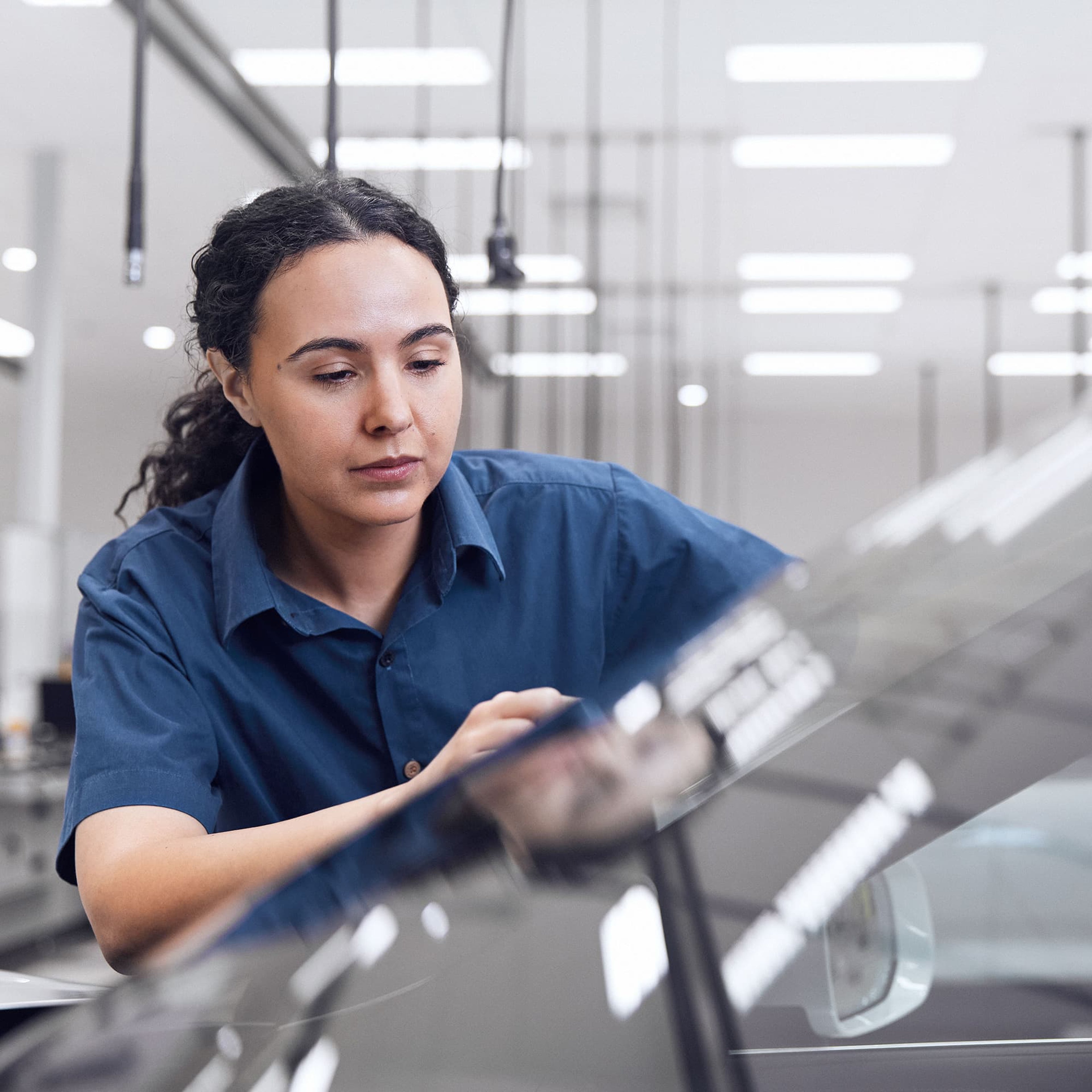 Une mécanicienne Volvo en uniforme bleue regarde attentivement le capot d'une Volvo recouvert de gouttelettes d'eau.