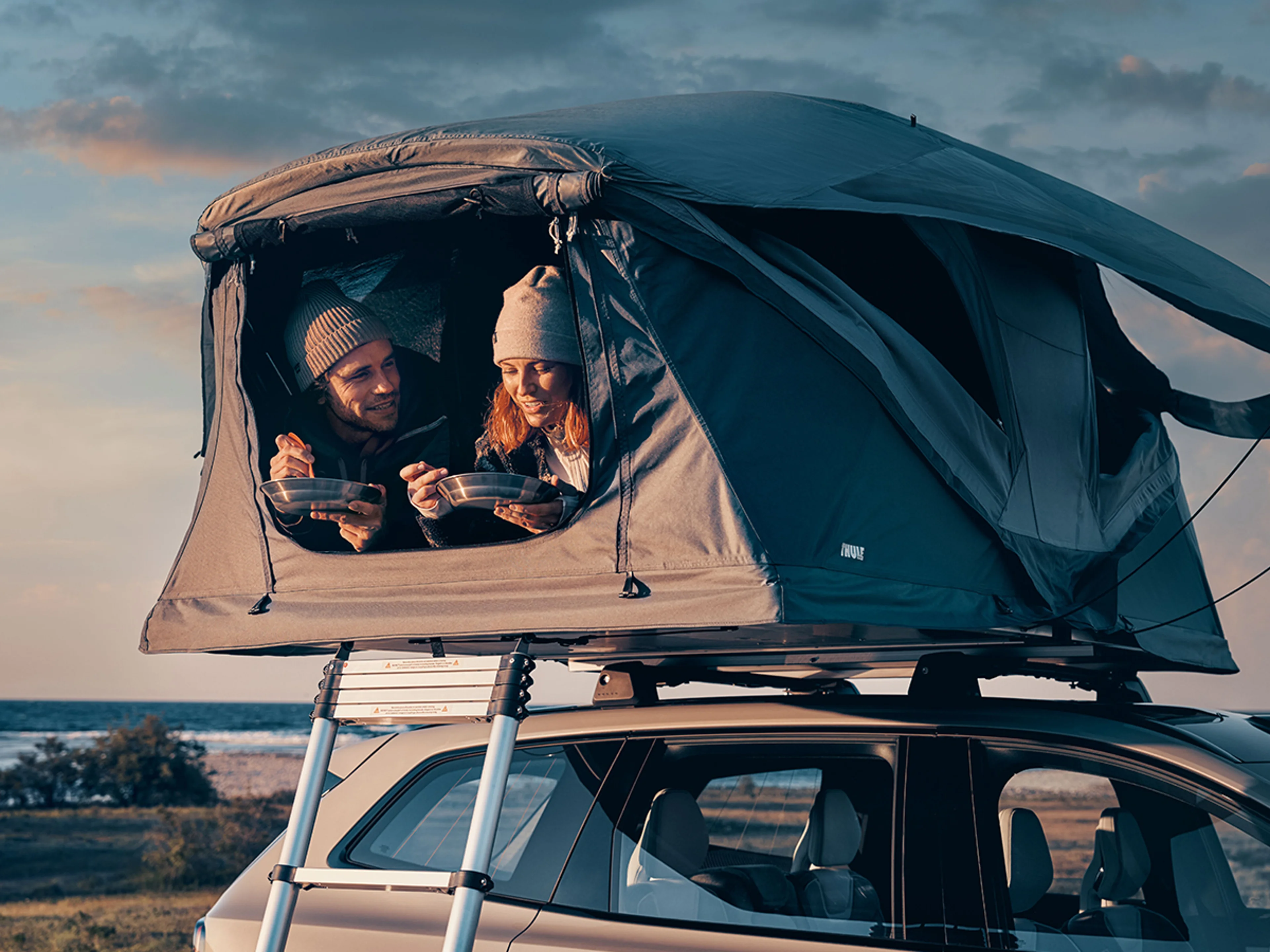 Två personer som äter i ett taktält på en parkerad Volvo.
