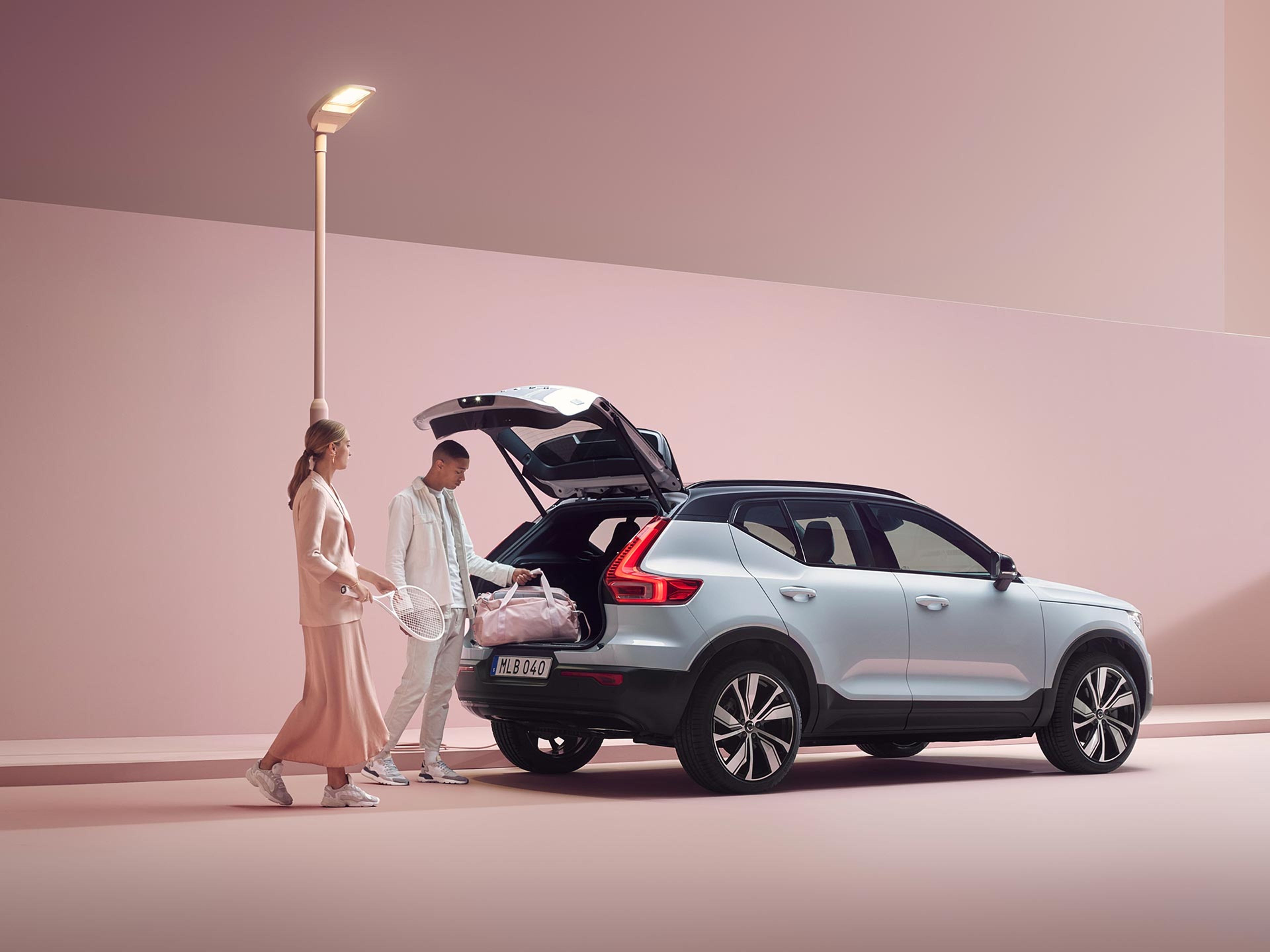 Eine Frau und ein Mann befüllen den Kofferraum eines silbernen Volvo XC40 mit Tennisausrüstungsartikeln.
