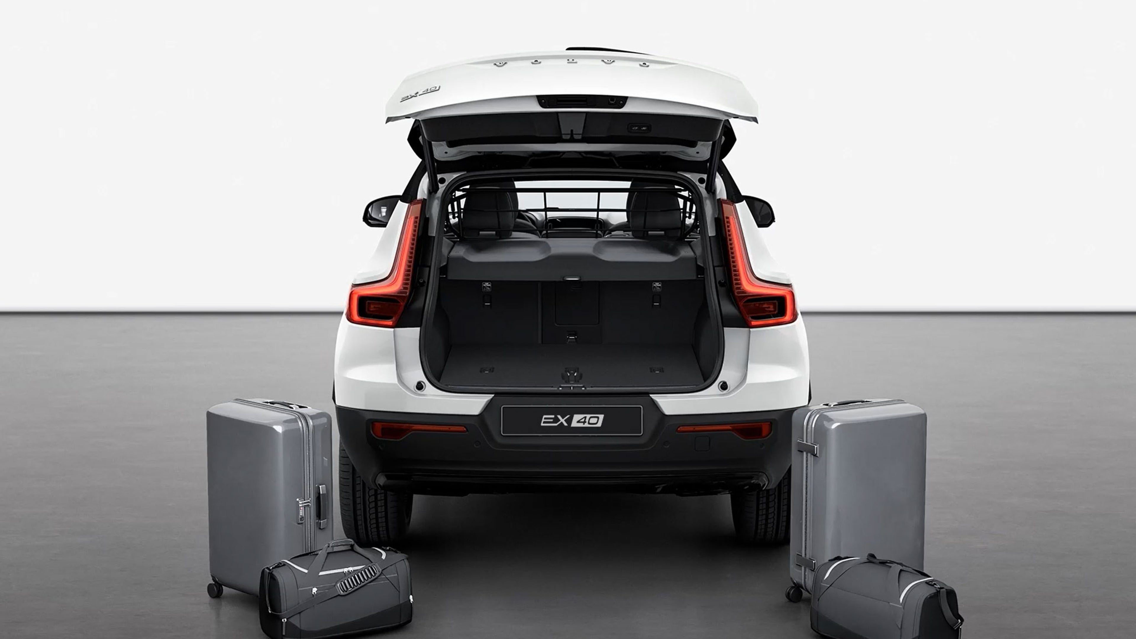 Vue arrière d’un Volvo EX40 blanc avec coffre ouvert, montrant l’espace de chargement et trois bagages au sol