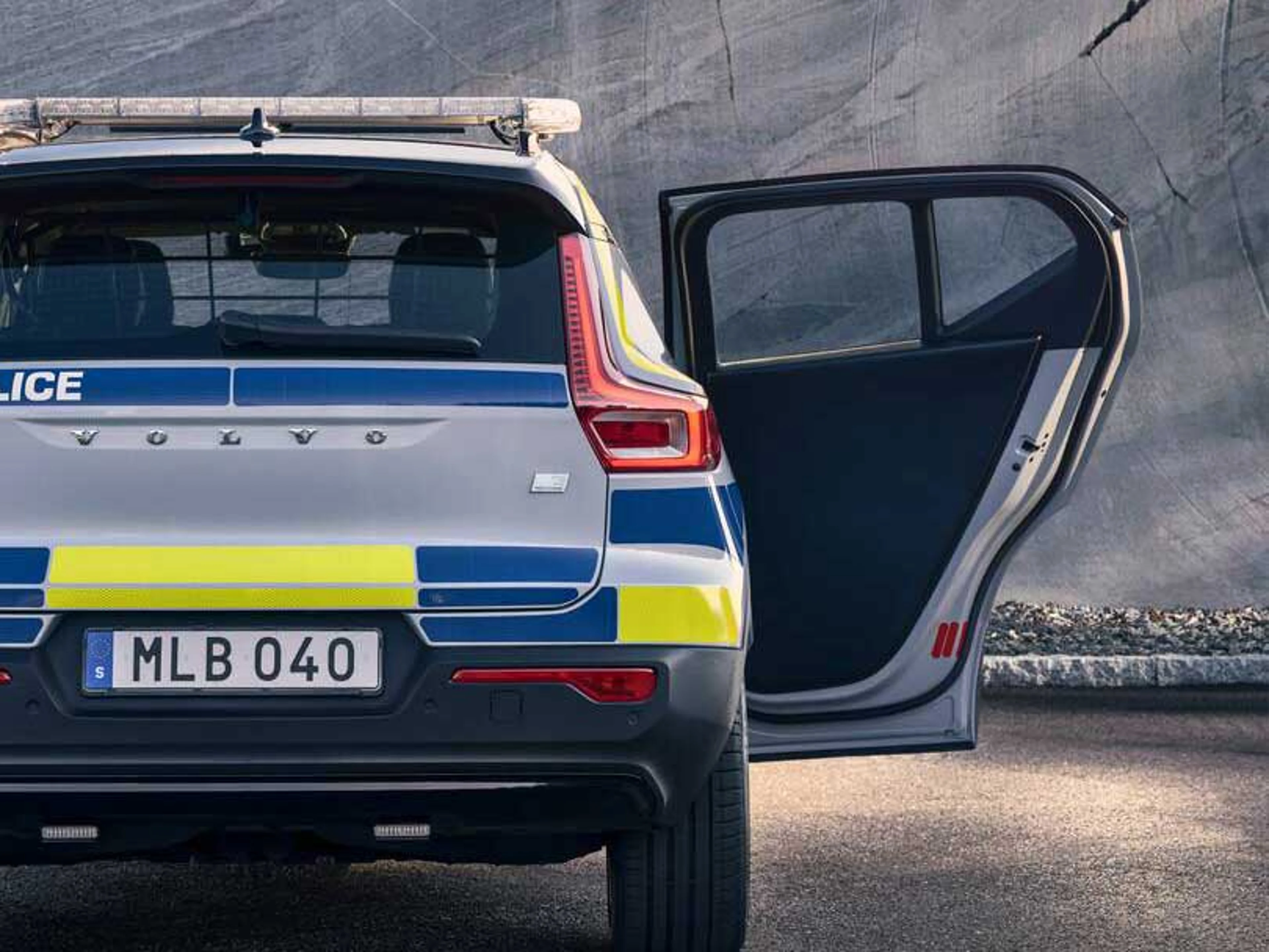 En bil fra Volvo med politimærkater ses bagfra med en åben passagerdør i et ødelagt gråt blok miljø