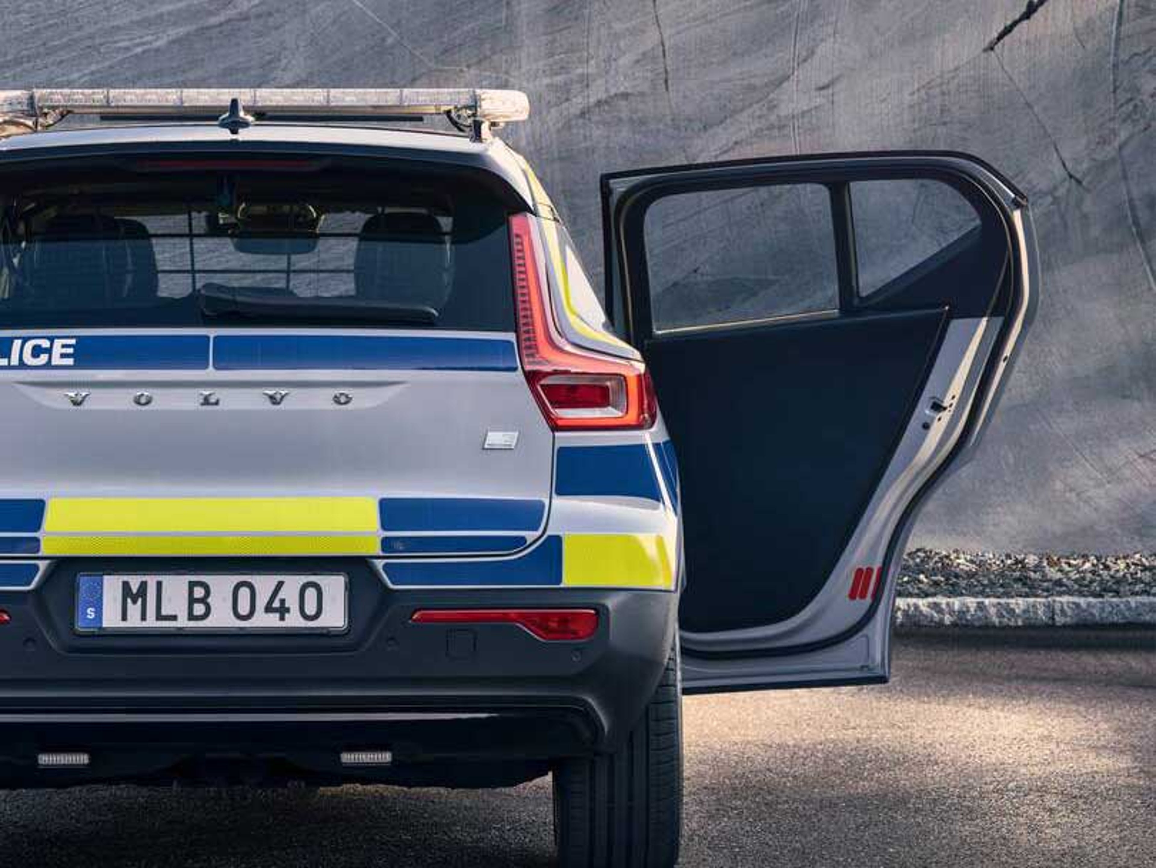 En bil fra Volvo med politimærkater ses bagfra med en åben passagerdør i et ødelagt gråt blok miljø