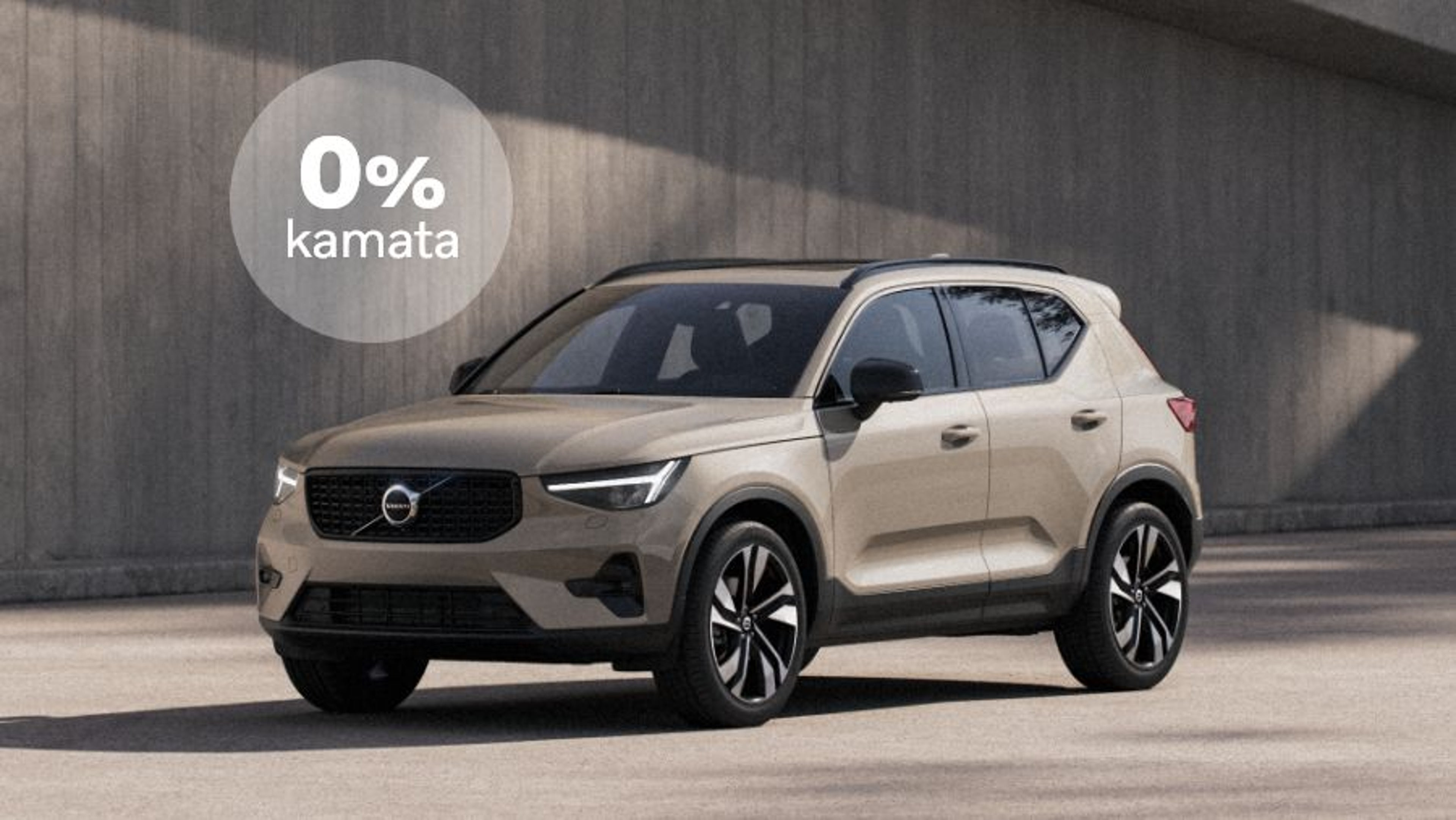 Bež Volvo XC40 SUV parkiran ispred betonskog zida na dnevnom svjetlu, s plavim krugom u gornjem desnom kutu na kojem piše "0% kamata"