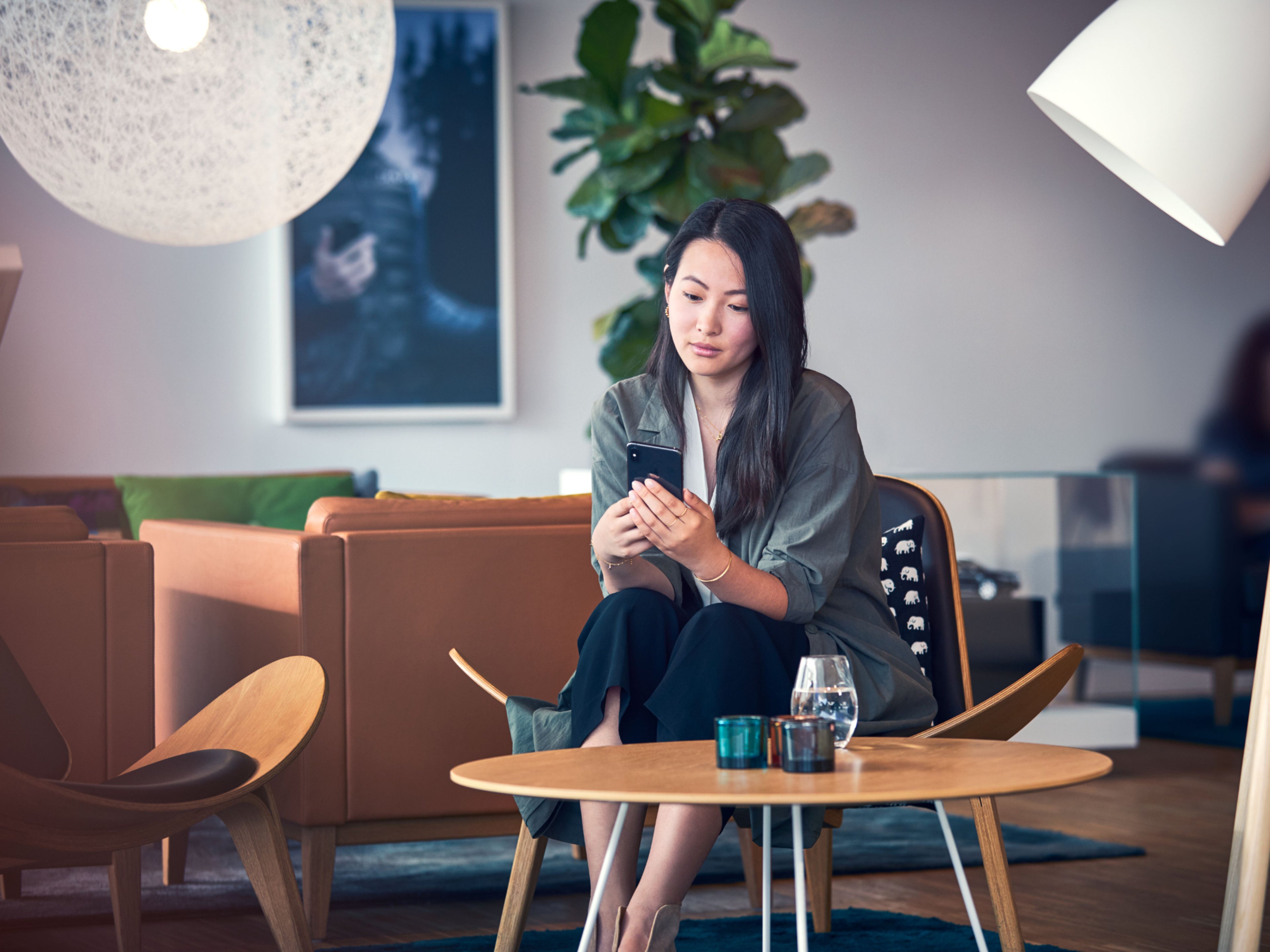 Eine Frau schaut auf ihr Handy. Sie sitzt in einer gemütlichen Lounge.