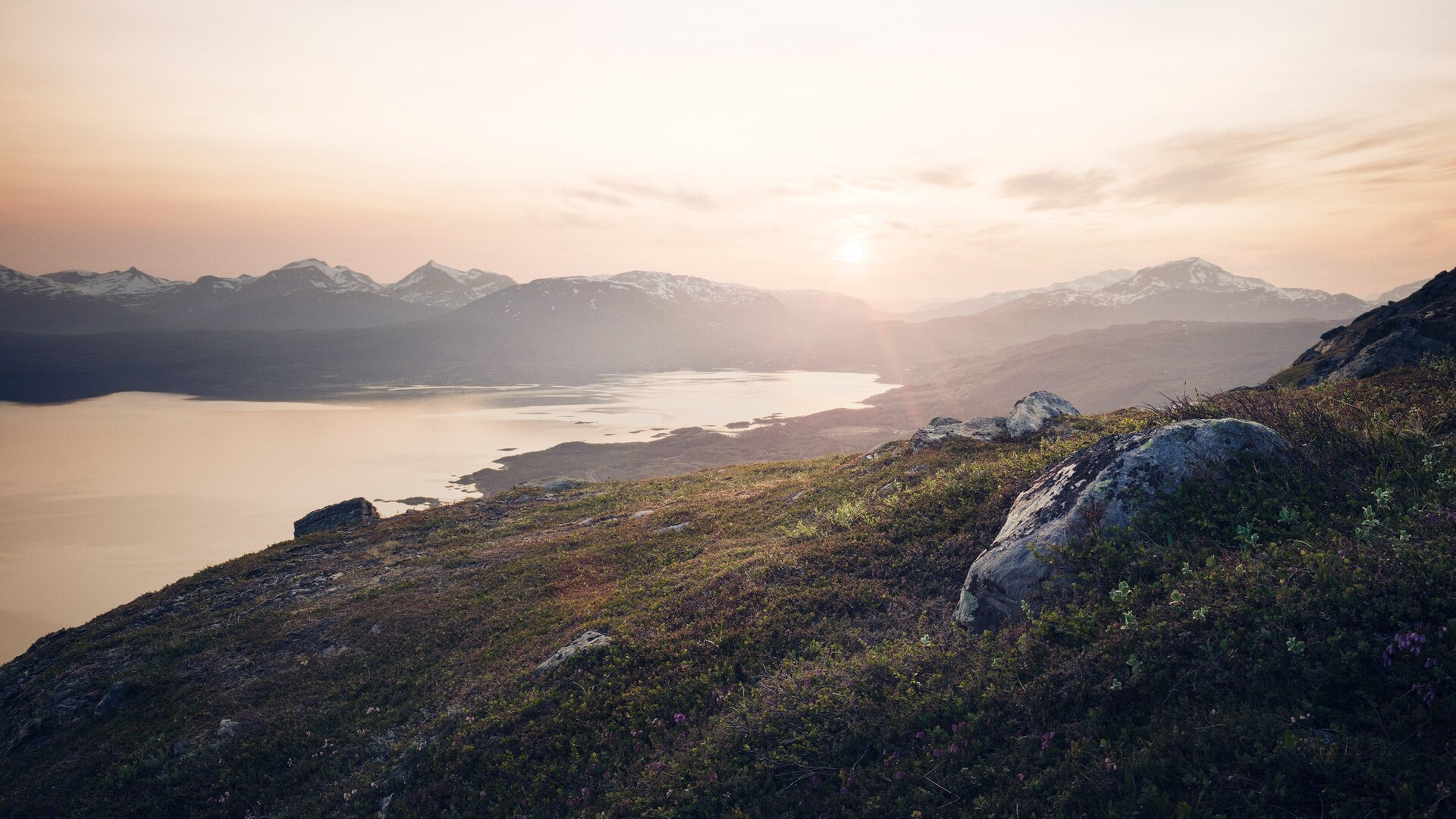 Skandinavisk kystlandskab med bjerge og hav, badet i sollys fra baggrunden