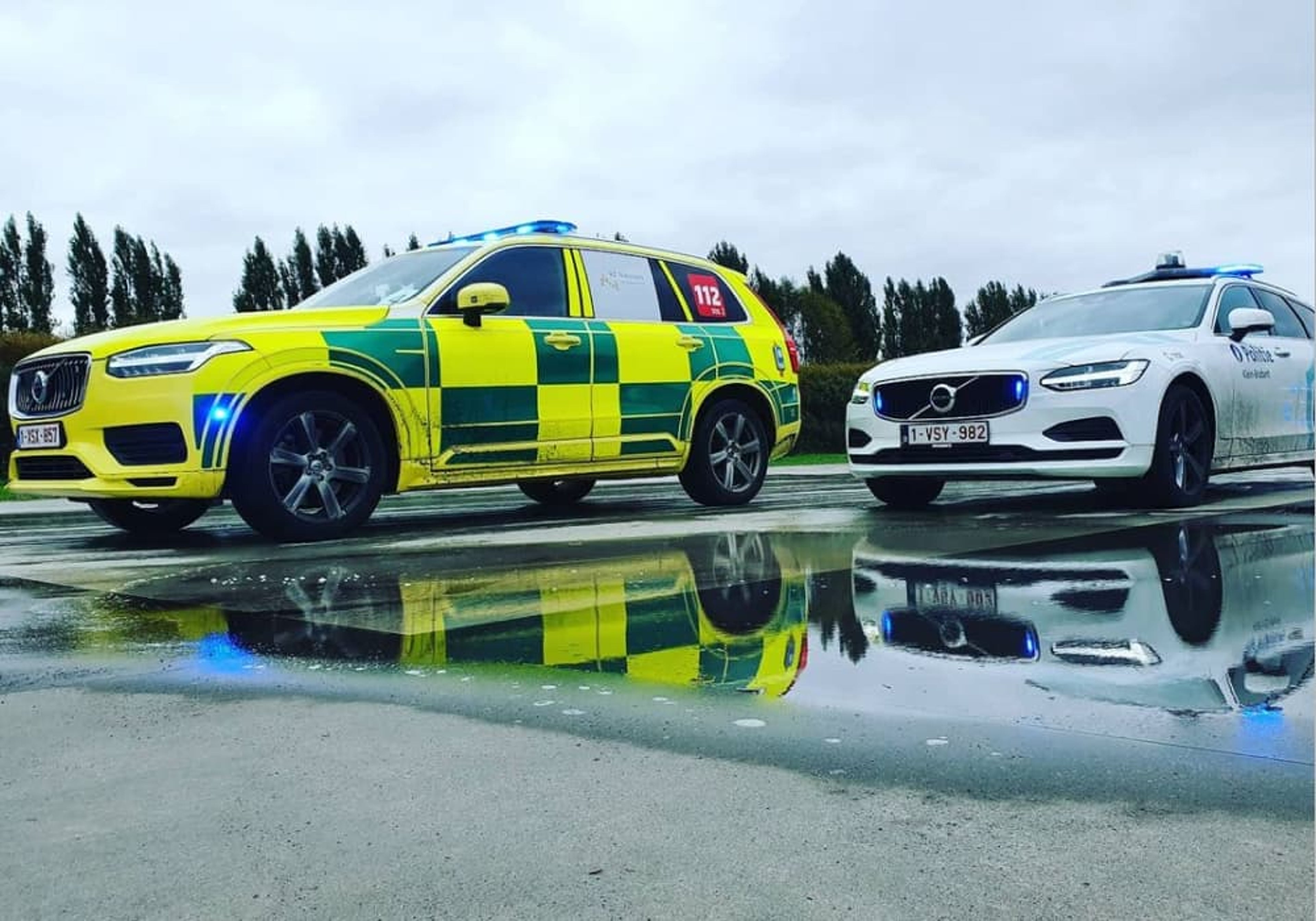 Un SMUR et une voiture de police sont garés l'un derrière l'autre, avec les reflets des voitures sur la chaussée mouillée.