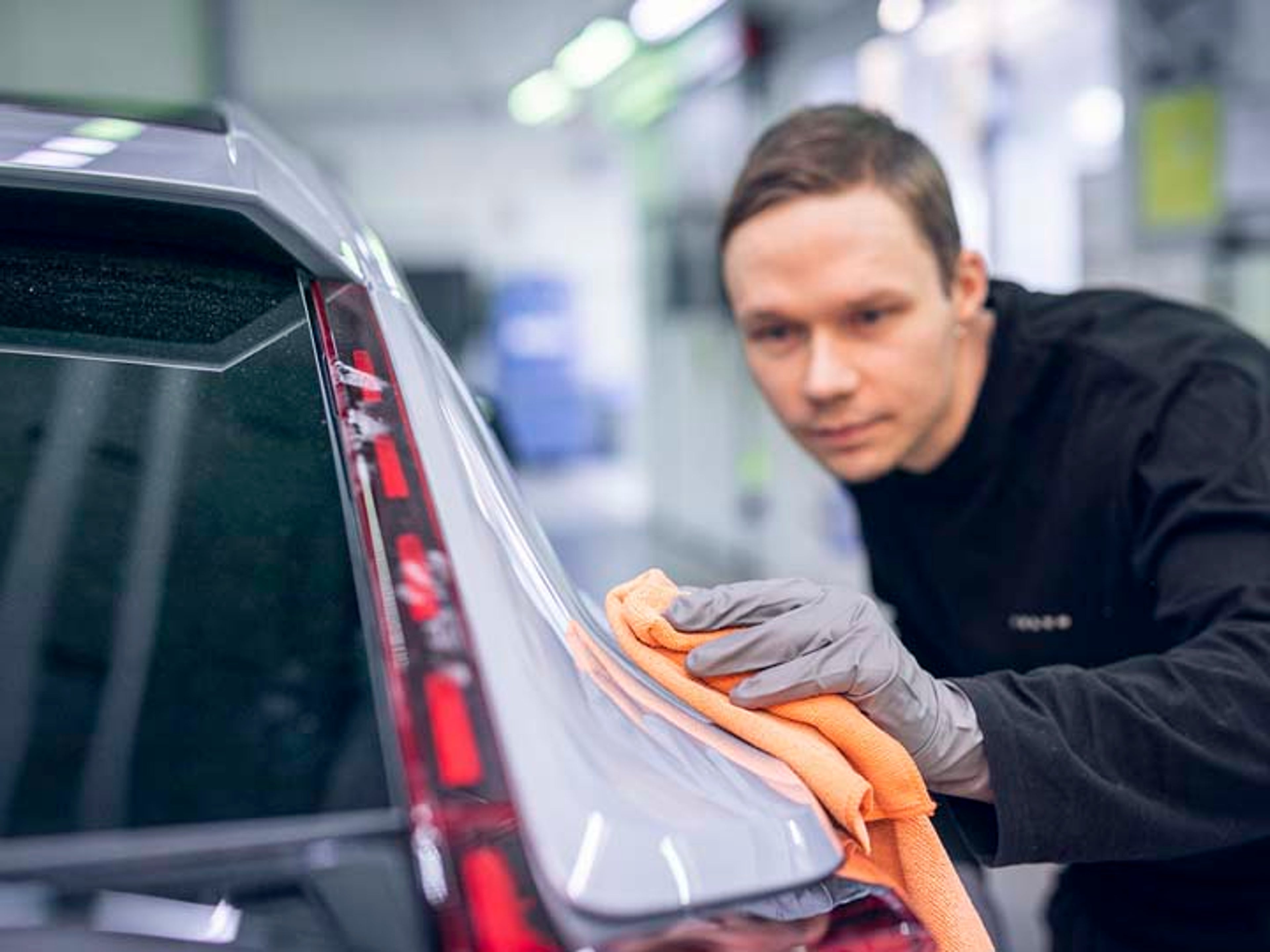 Un hombre limpiando con una gamuza y mucho cuidado la carrocería de un vehículo Volvo