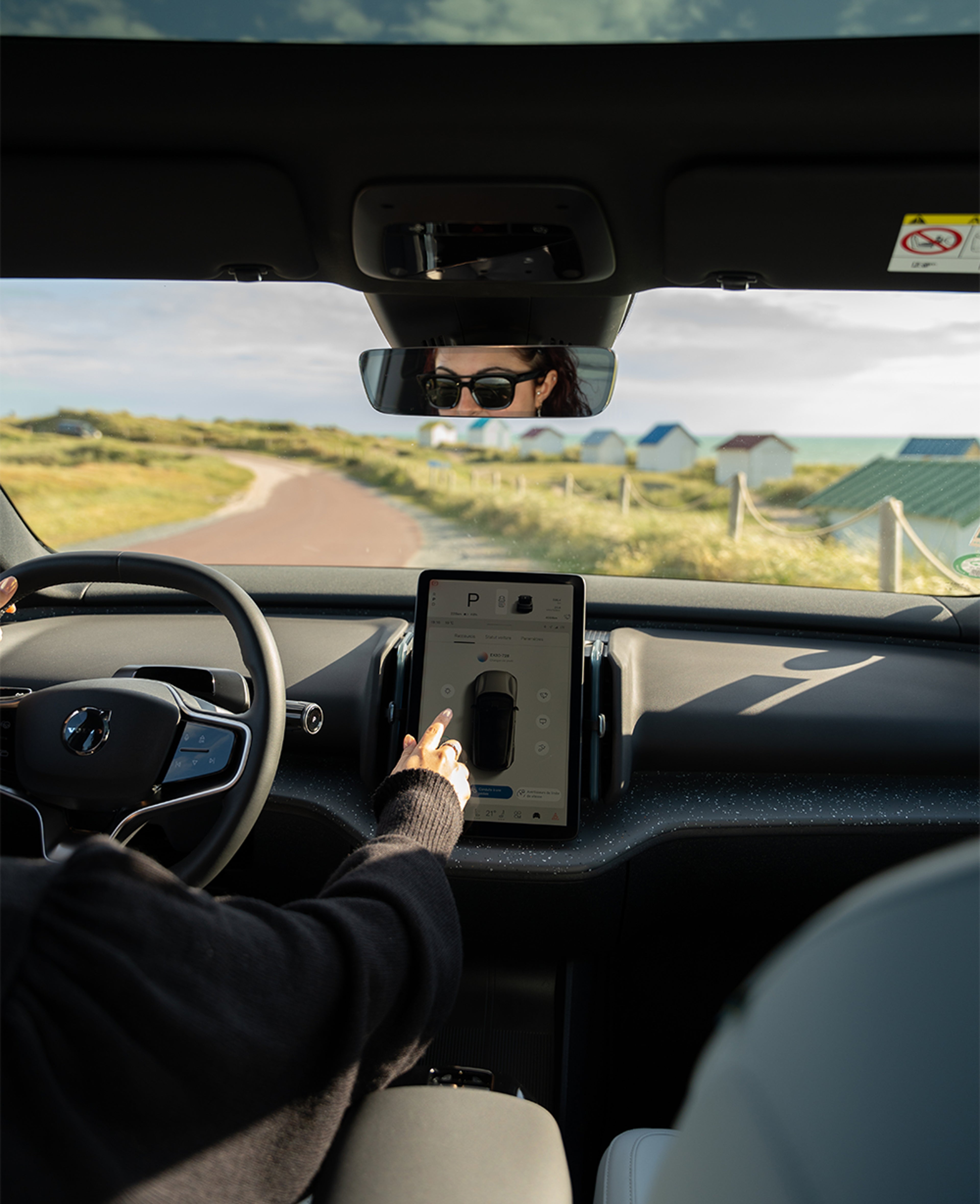 Intérieur de voiture, personne touchant l’écran tactile, route de campagne visible par le pare-brise.