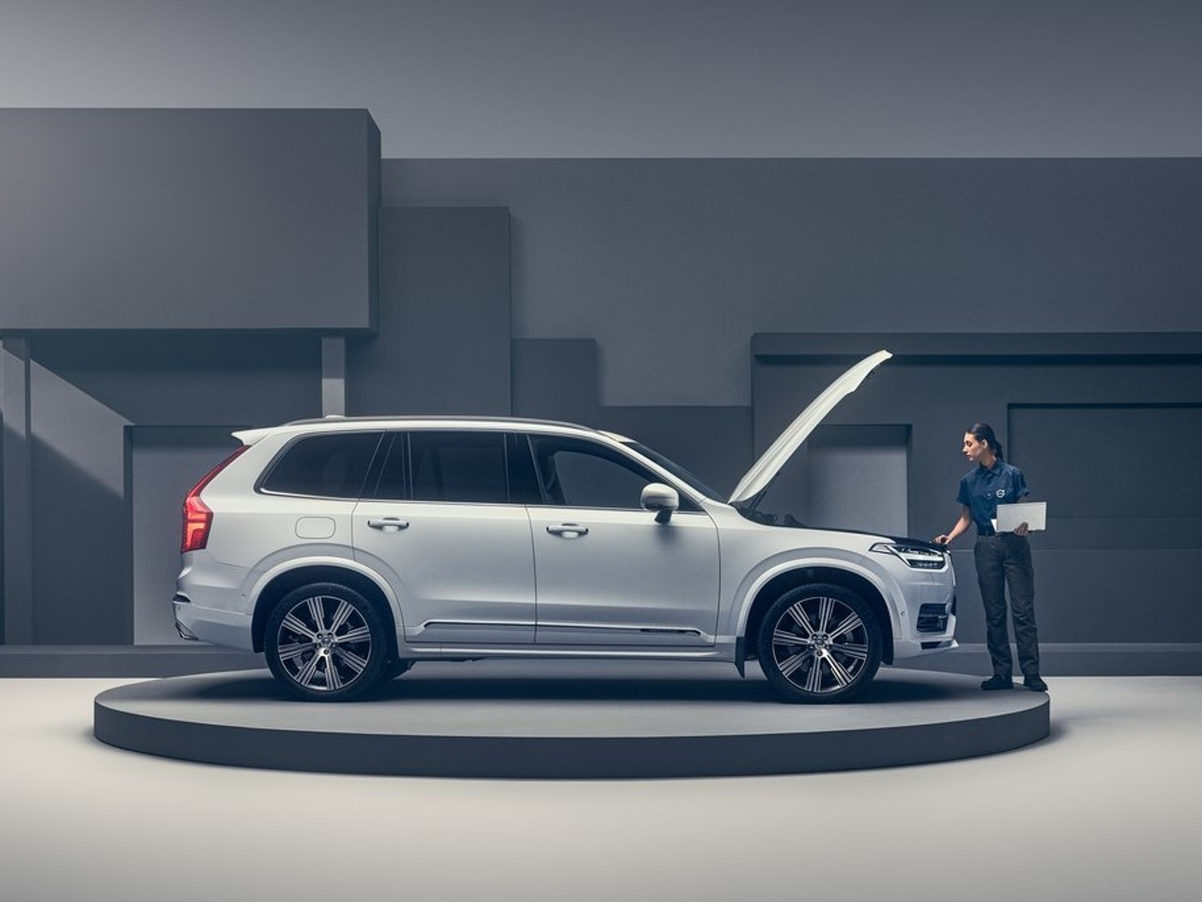 Bir kadın teknisyenin üzerinde çalıştığı yükseltilmiş kaputlu beyaz Volvo.