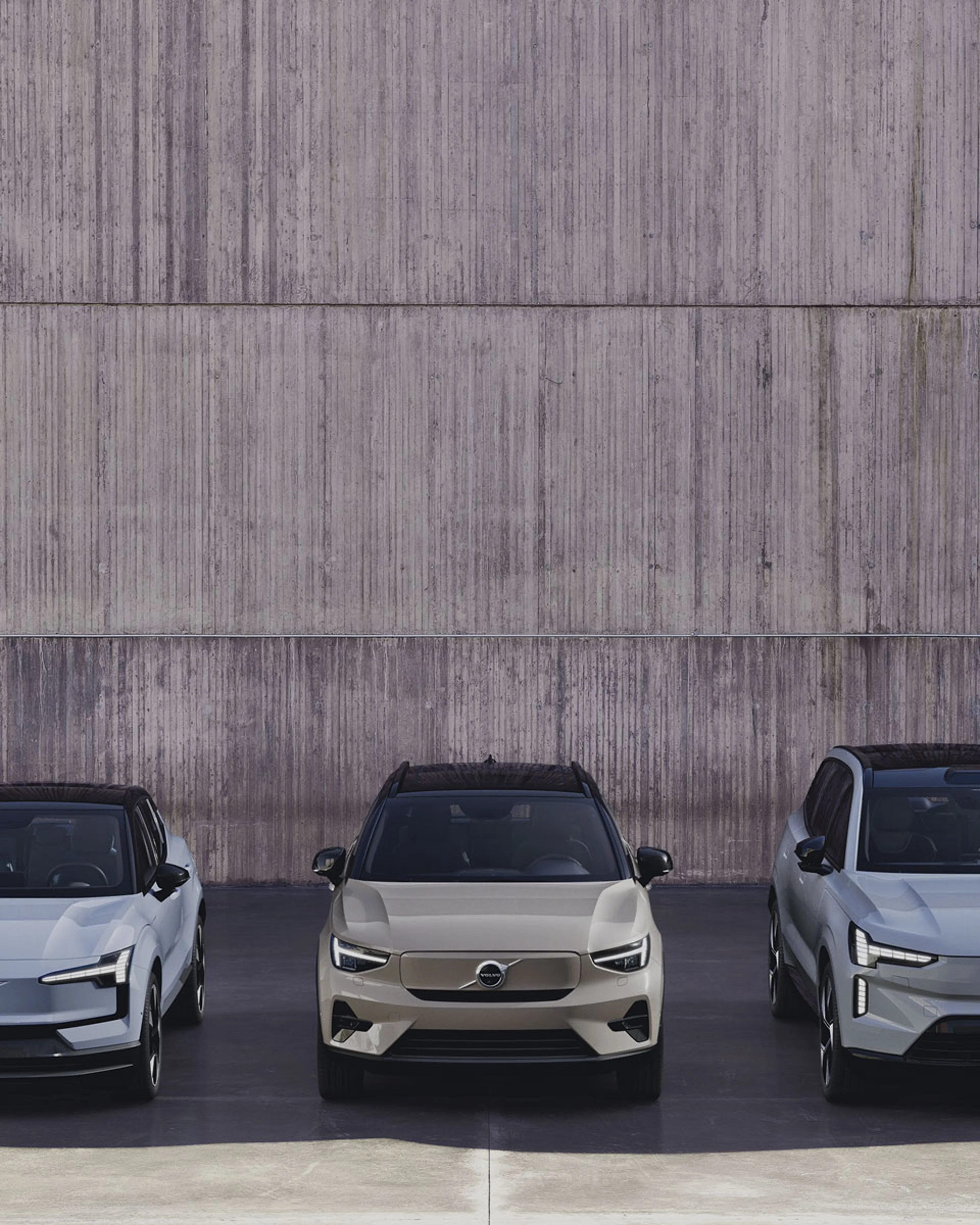 Une Volvo EX30, une EX40 et une EX90 sont garées devant un mur en béton.