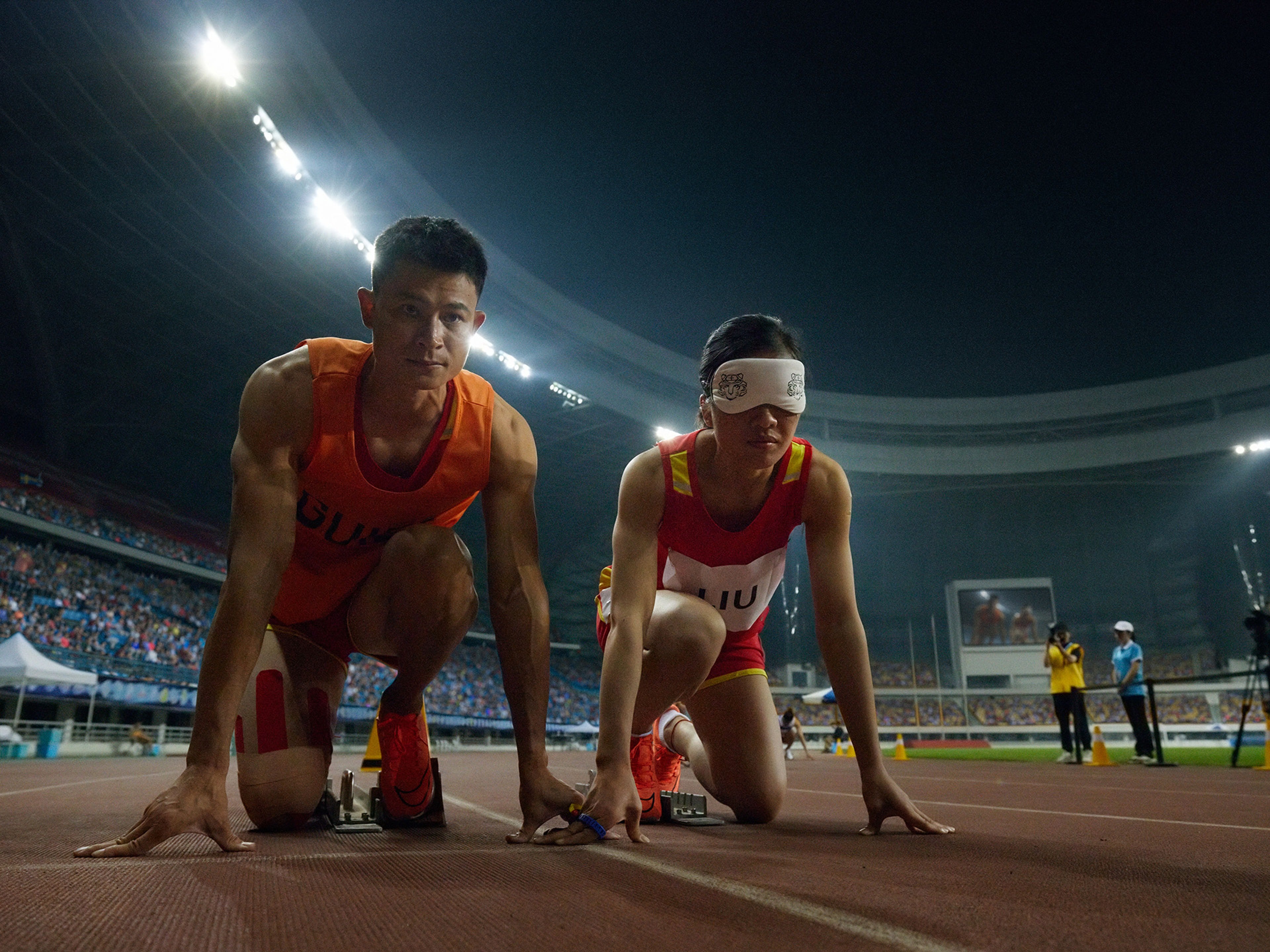 Liu Cuiqing e o seu guia Xu Donglin num estádio à noite, prontos para inicar uma corrida