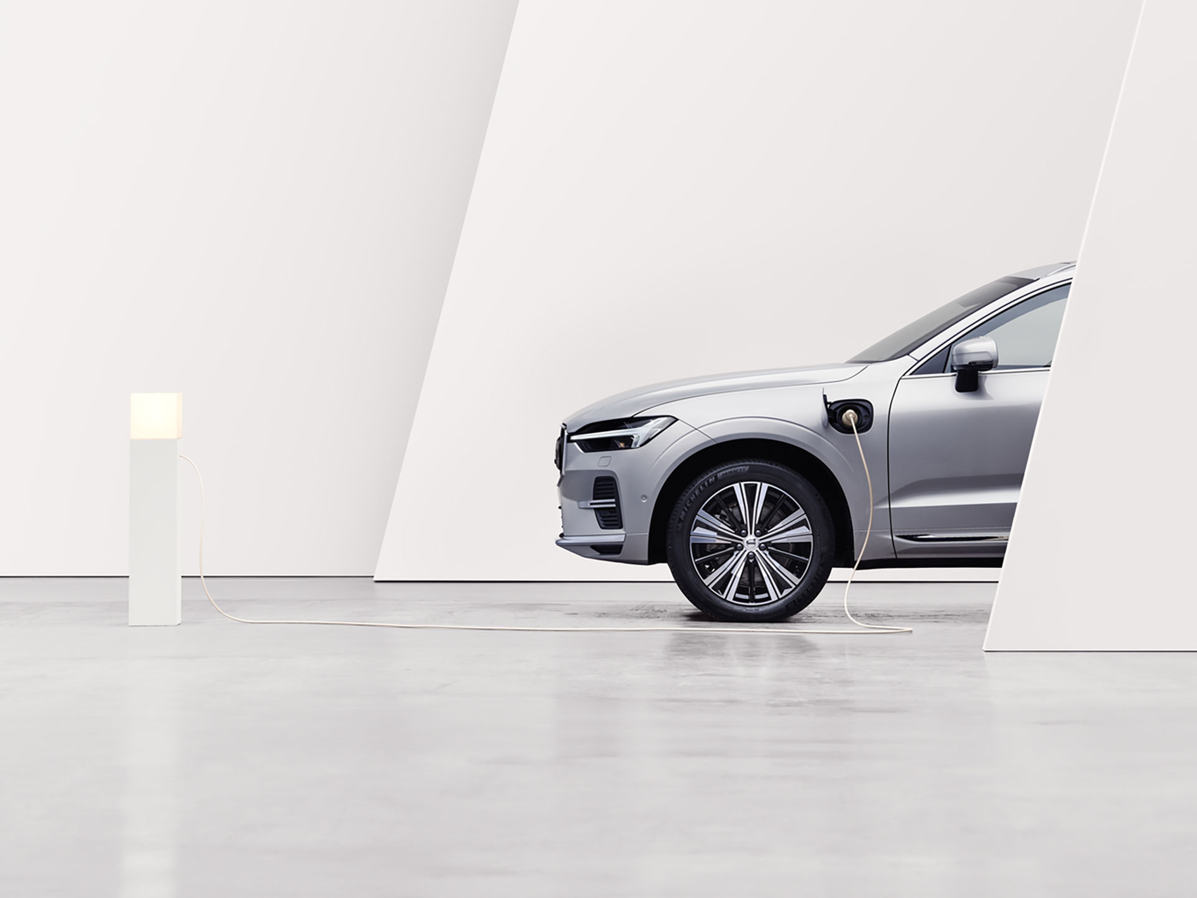 Voiture électrique Volvo grise en charge sur borne blanche, dans un cadre moderne et minimaliste.