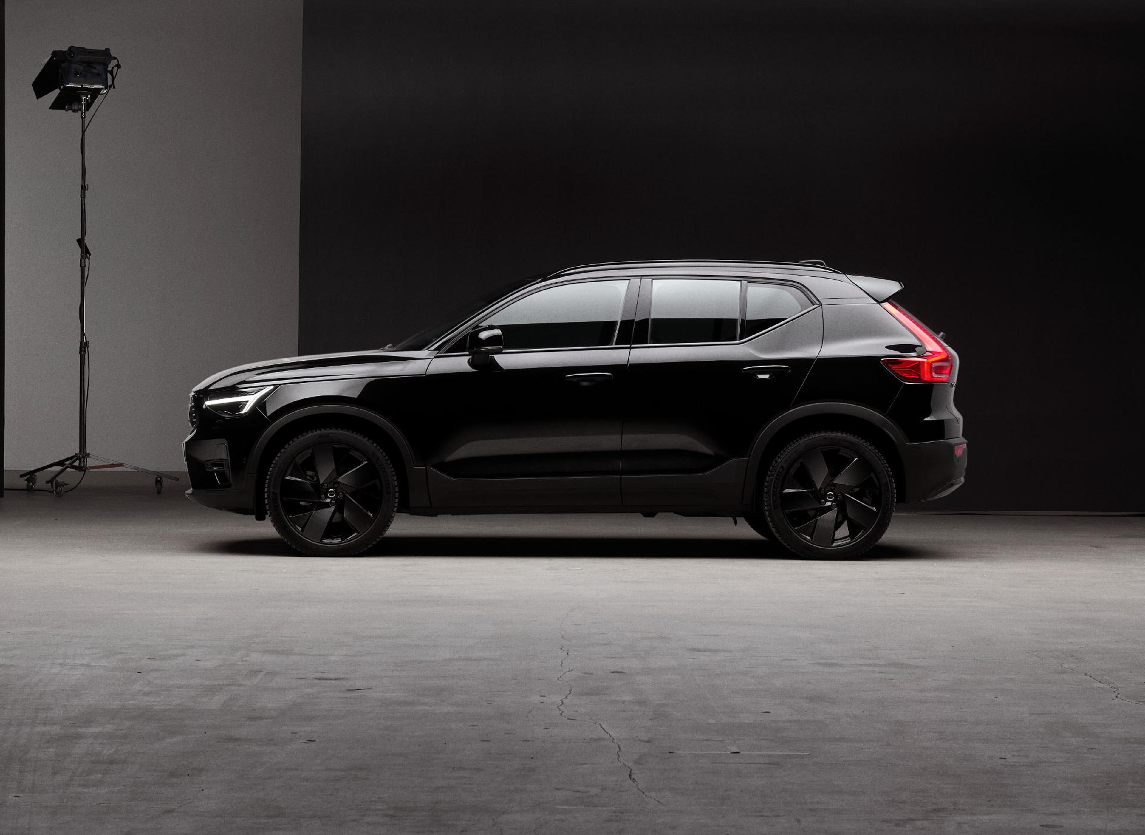 Seitenansicht eines tiefschwarzen Volvo XC40 SUV vor einer schwarzen Wand.