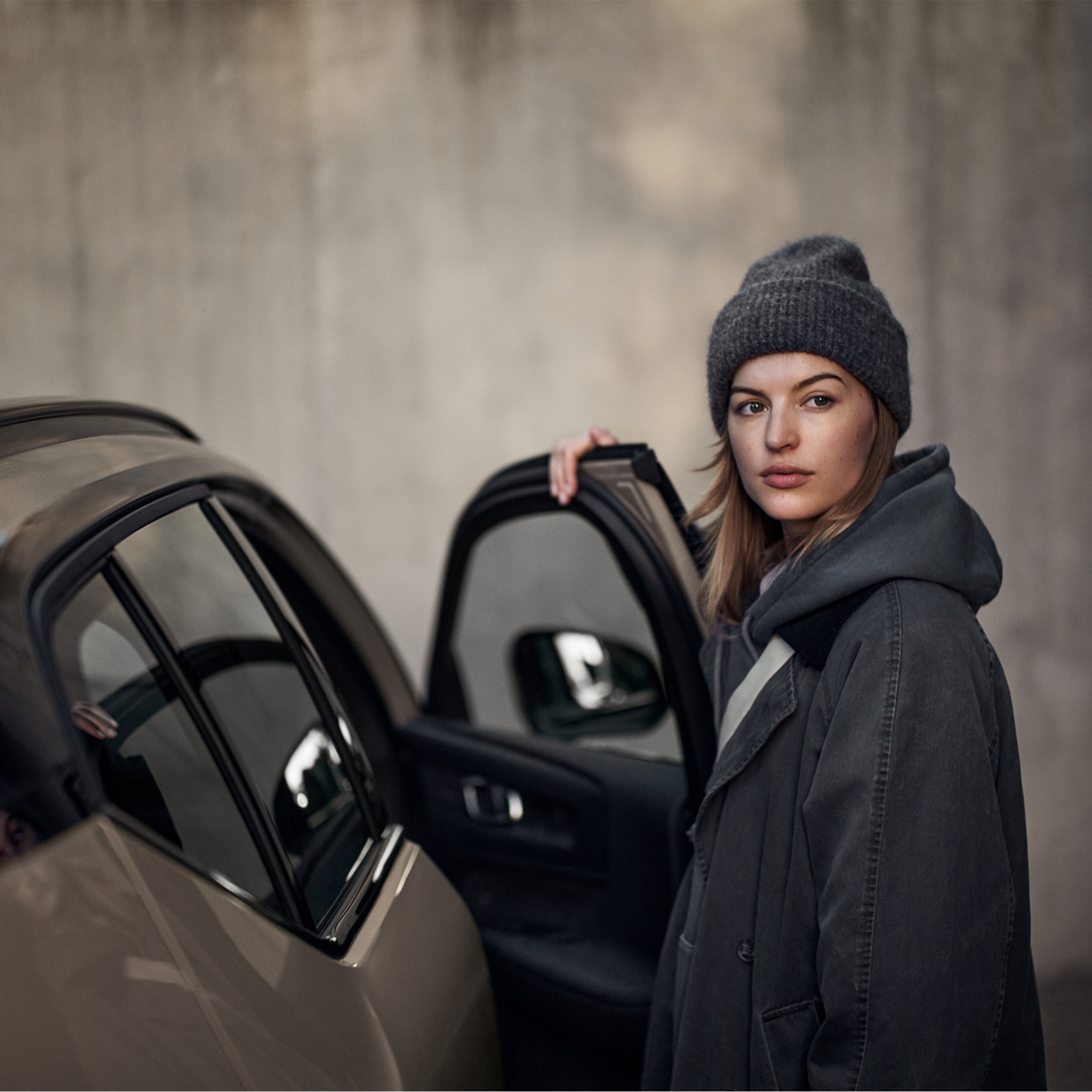 Nainen seisoo Volvo EX40 sähköauton avonaisen oven vieressä ja katsoo olan yli.