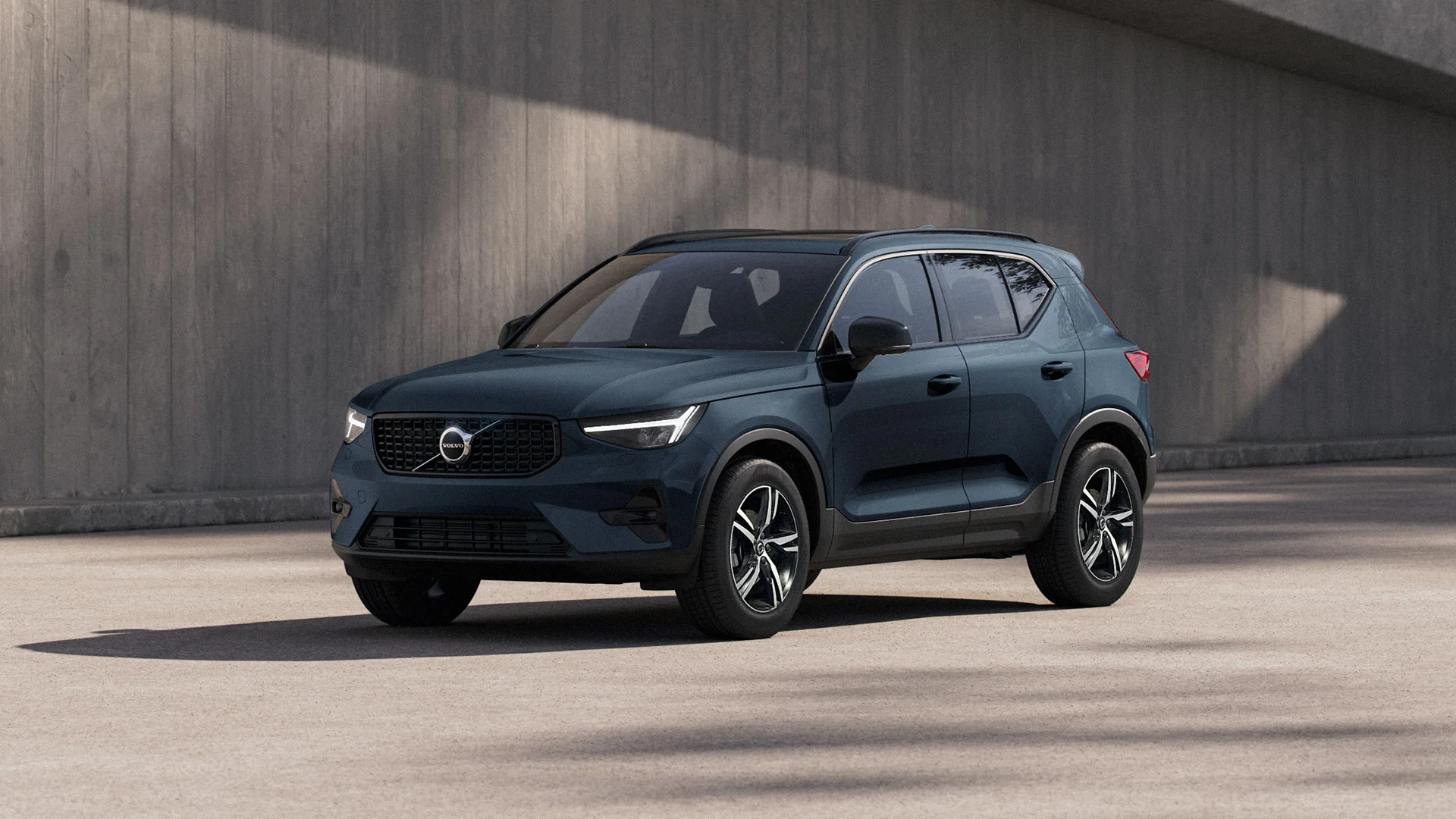 Volvo XC40 bleu foncé garé sur du béton, avec un grand mur en béton en arrière-plan