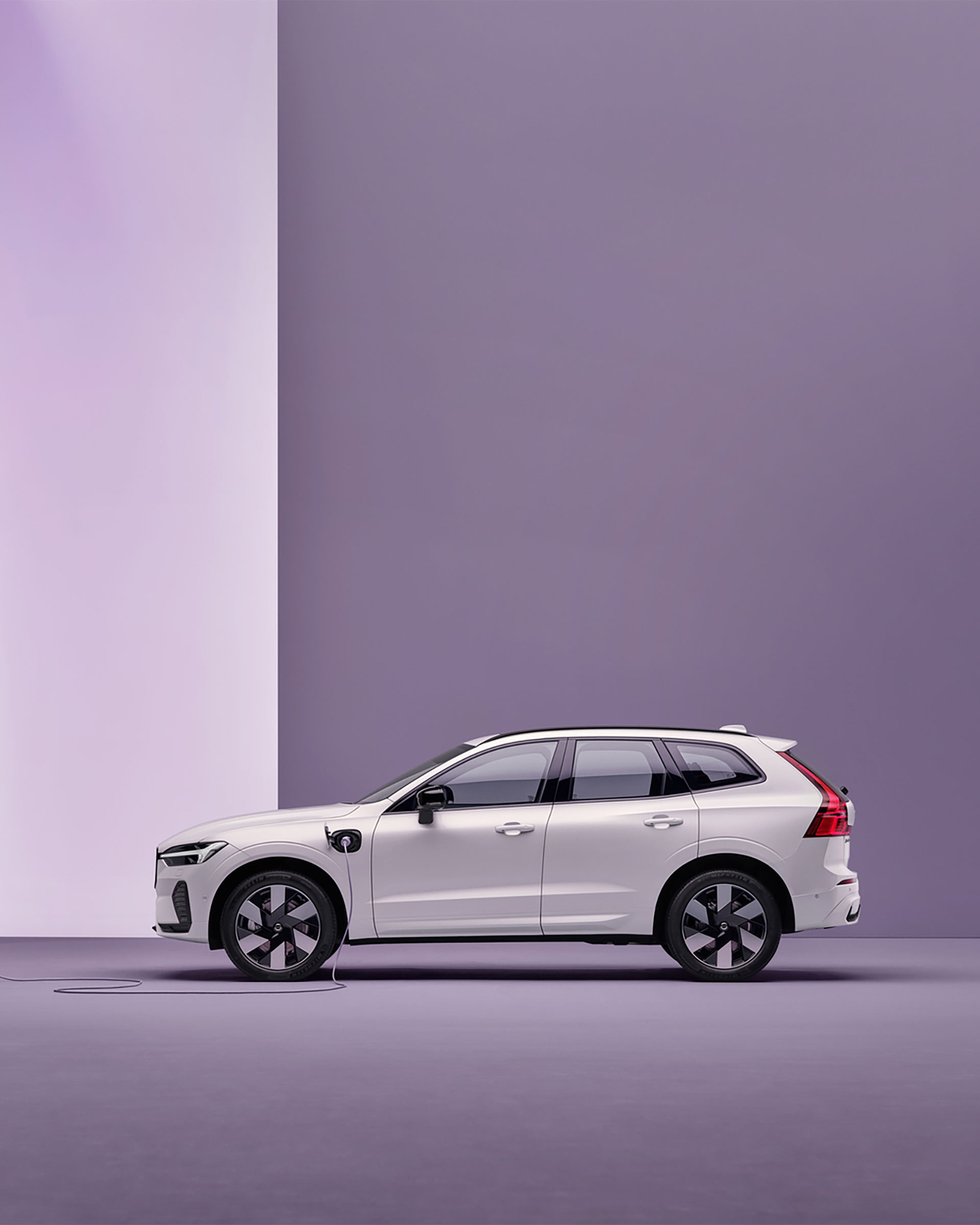 SUV blanc vu de profil, garé devant un mur violet clair sur fond uni.