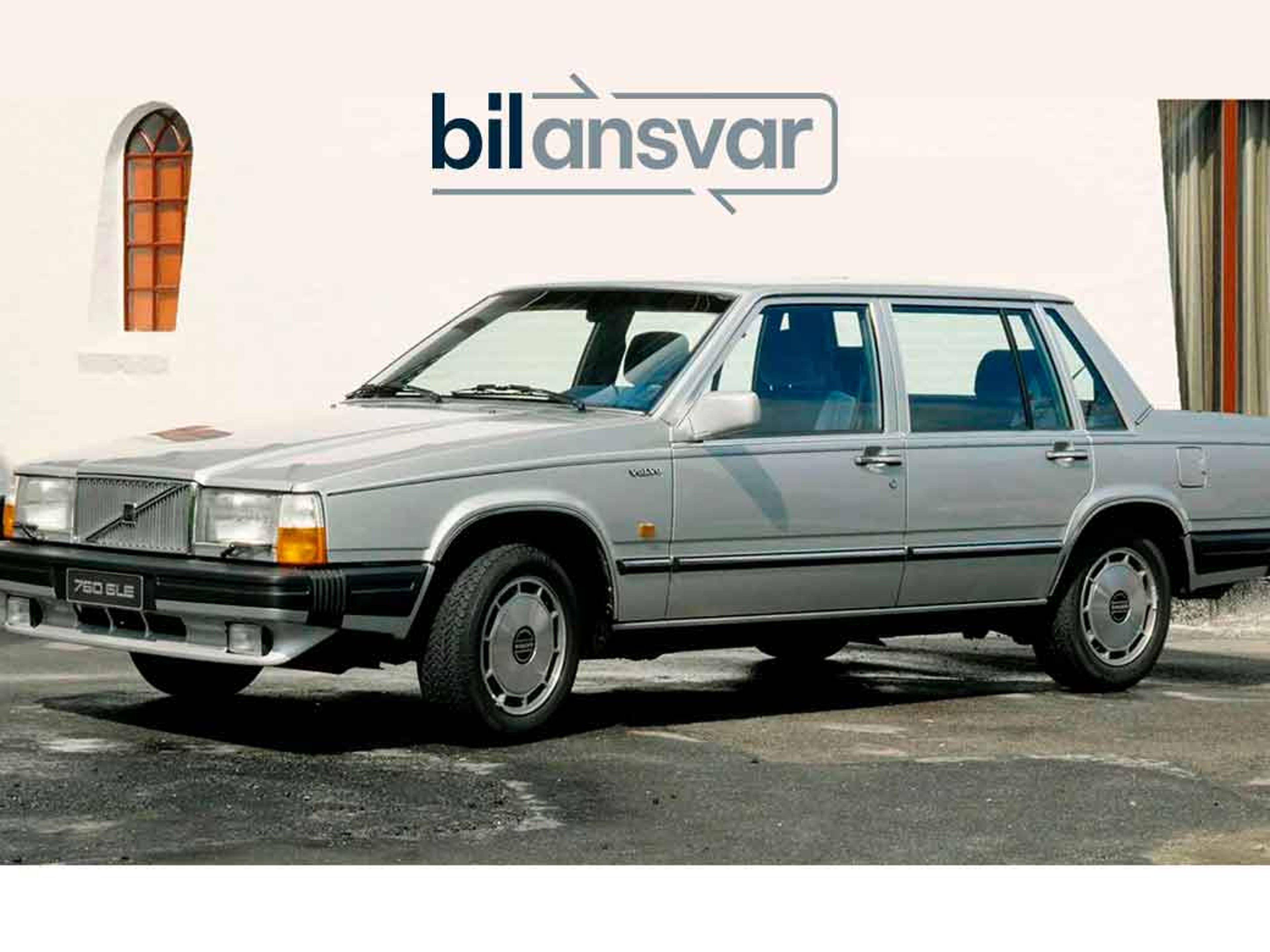 En sølvfarvet Volvo 760 GLE sedan holder parkeret foran en hvid mur med buede vinduer. Logoet og navnet "Bilansvar" er vist ovenover.