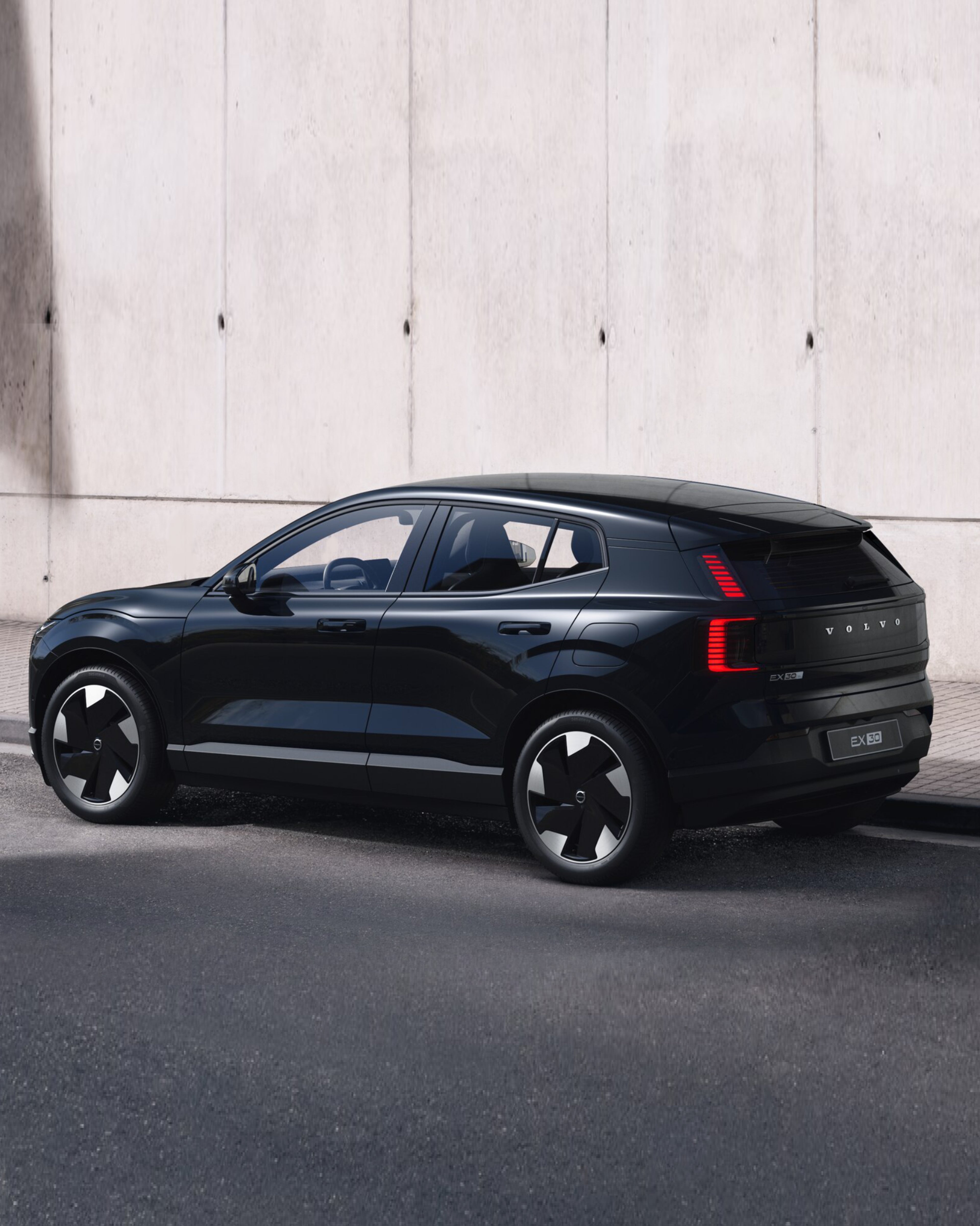 Seitliche Ansicht eines schwarzen Volvo EX30 vor einer hellen Steinwand.