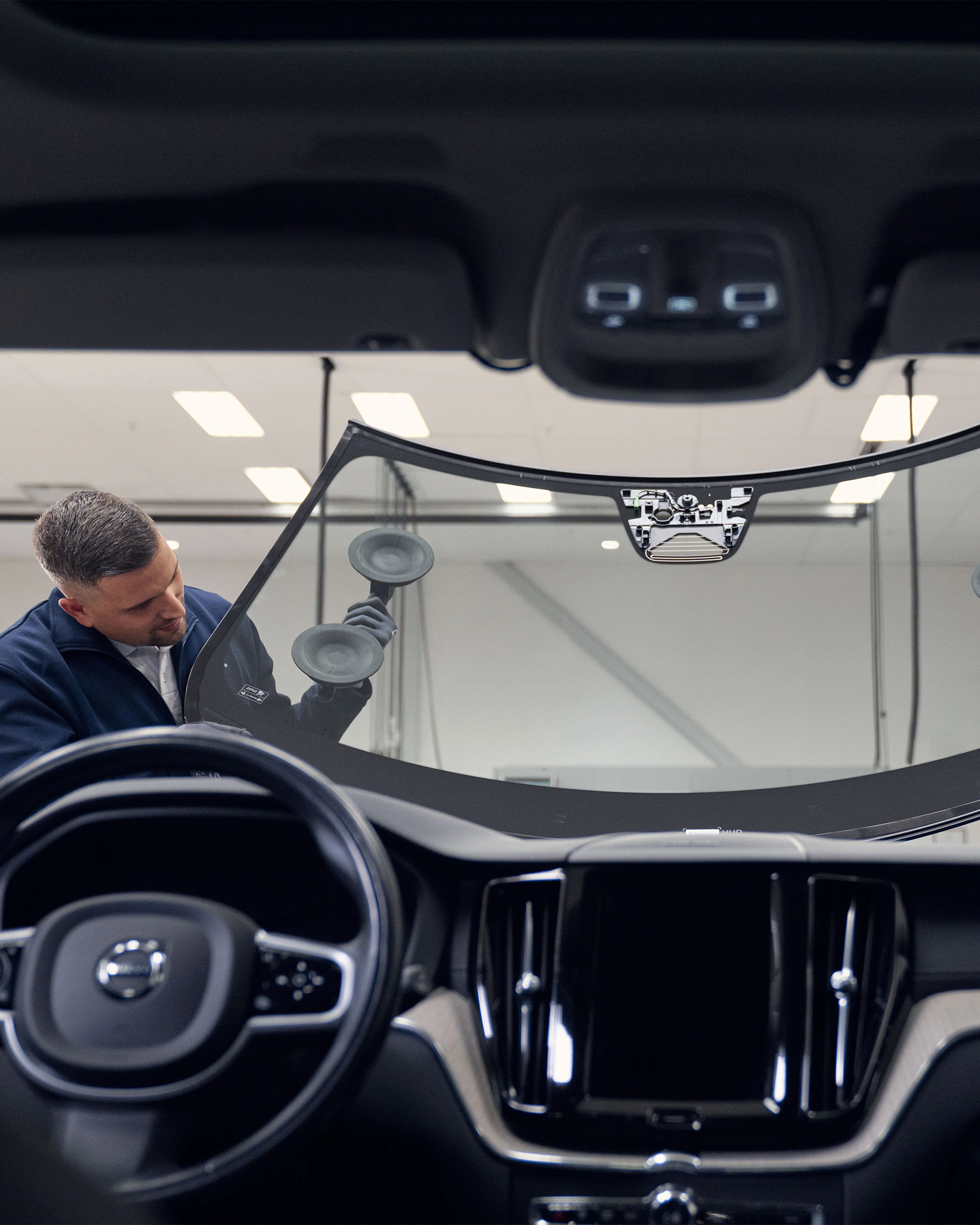 Deux techniciens installent un pare-brise sur une Volvo, vu de l’intérieur du véhicule.