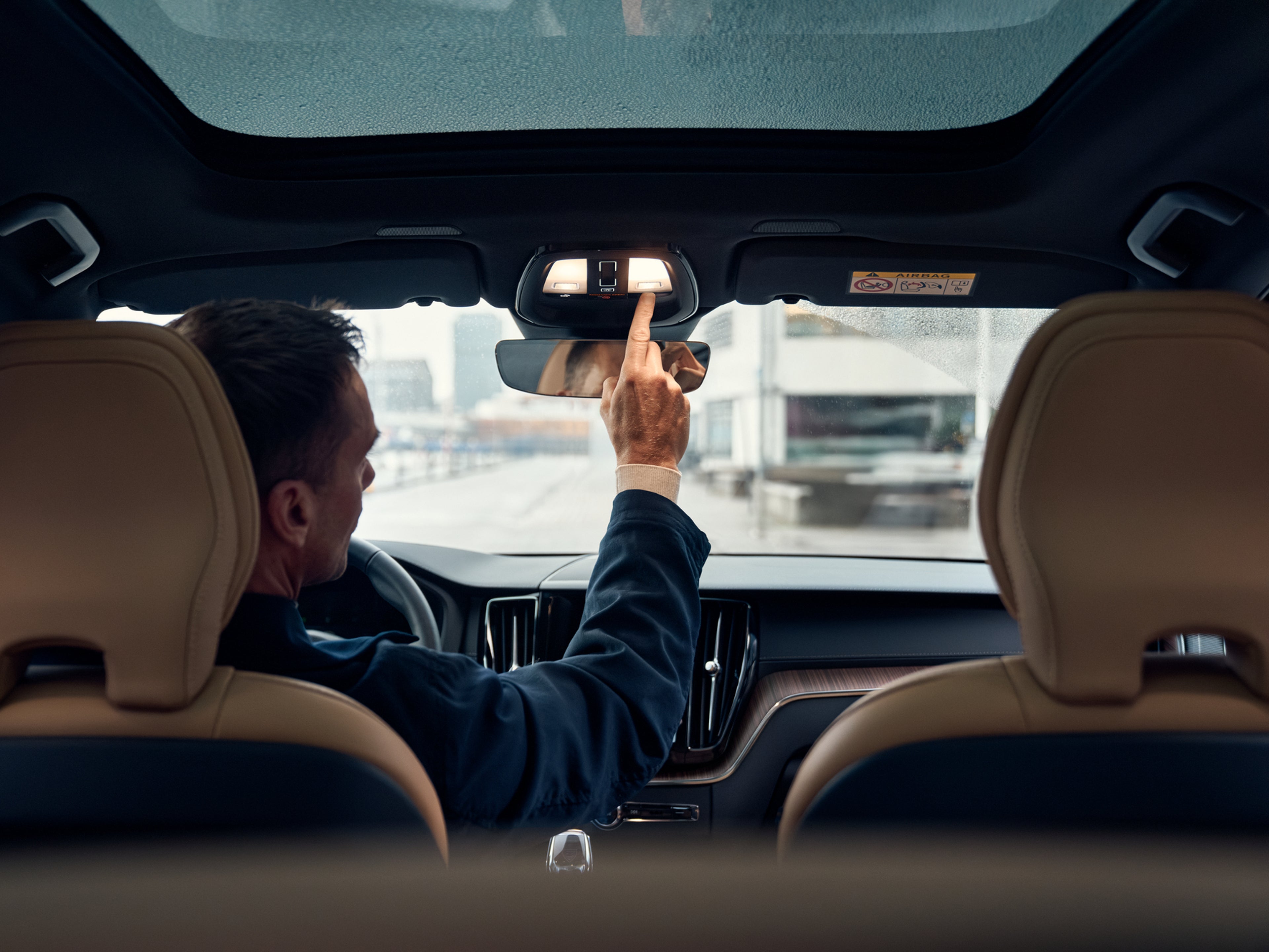 Man in driving seat of Volvo car reaching up to press roof console light switch