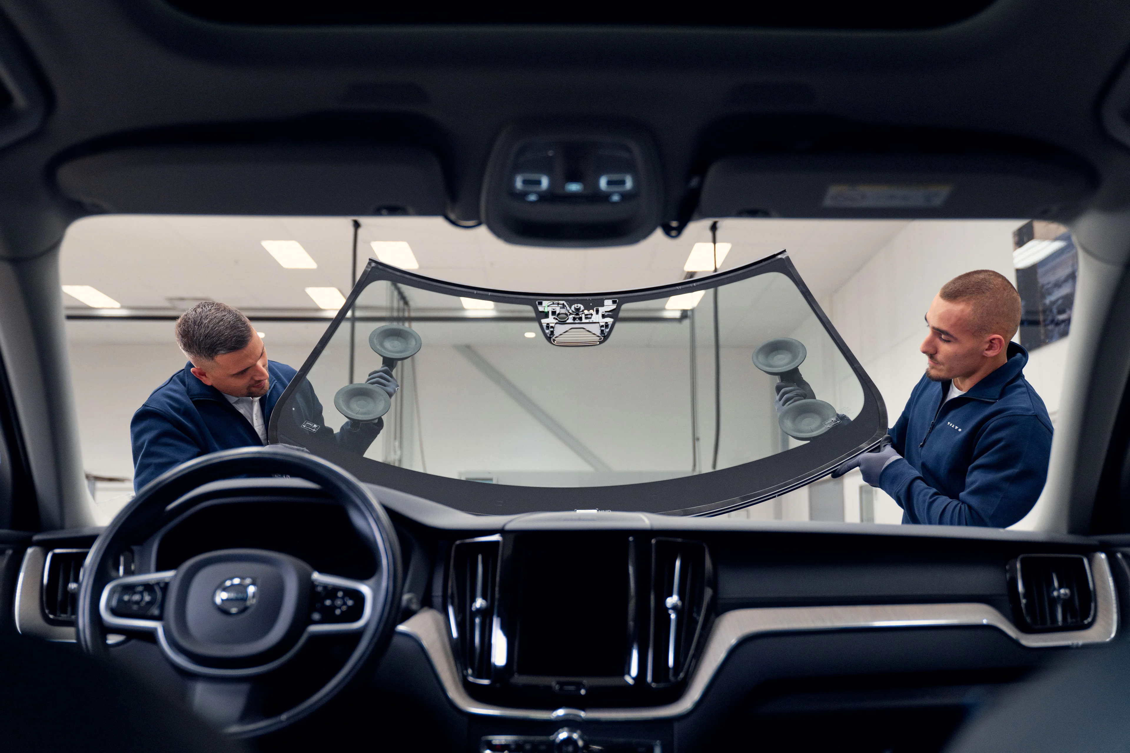 Twee monteurs plaatsen een nieuwe voorruit van een Volvo