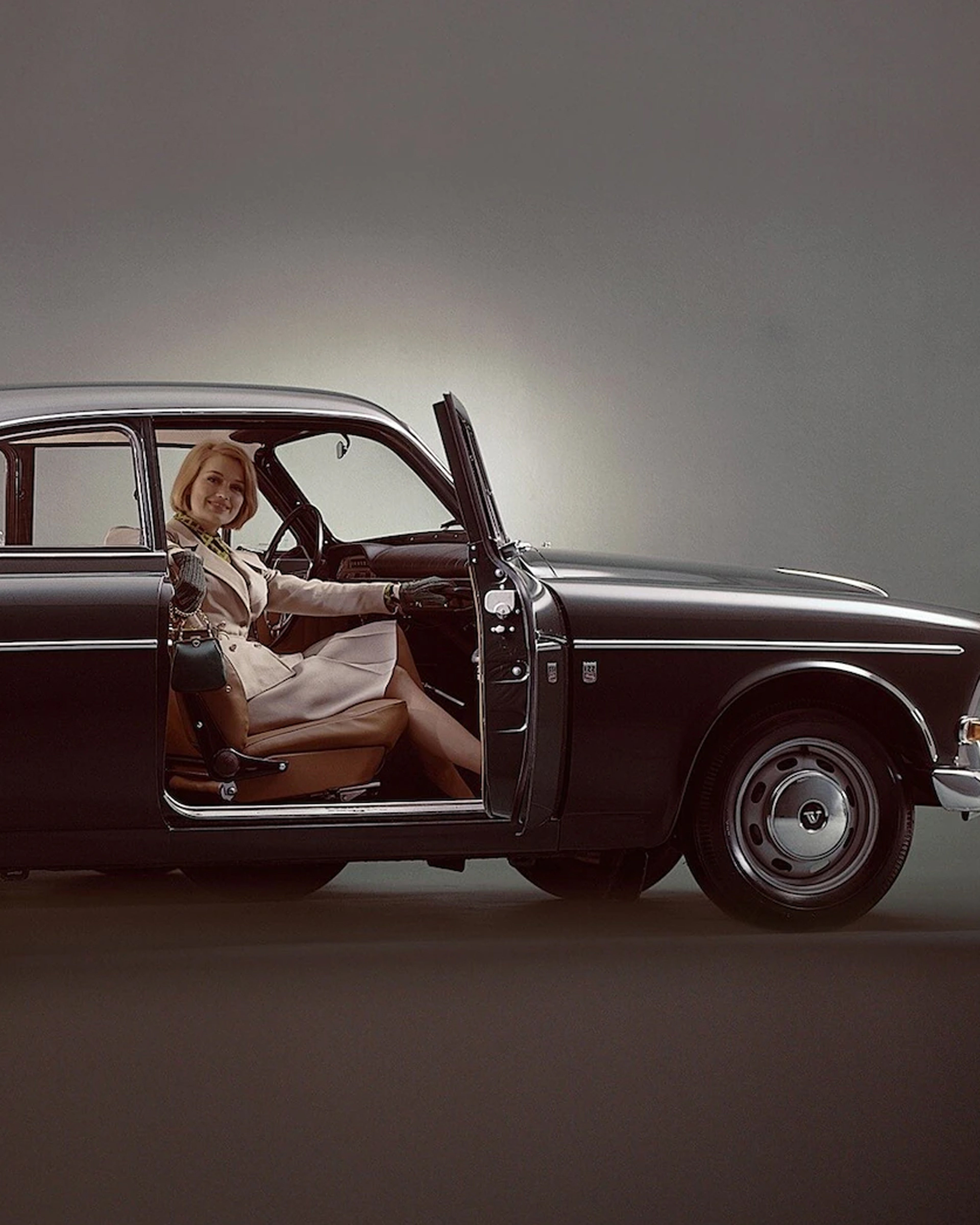 Dame som sitter i en eldre Volvo med døren åpen og smiler